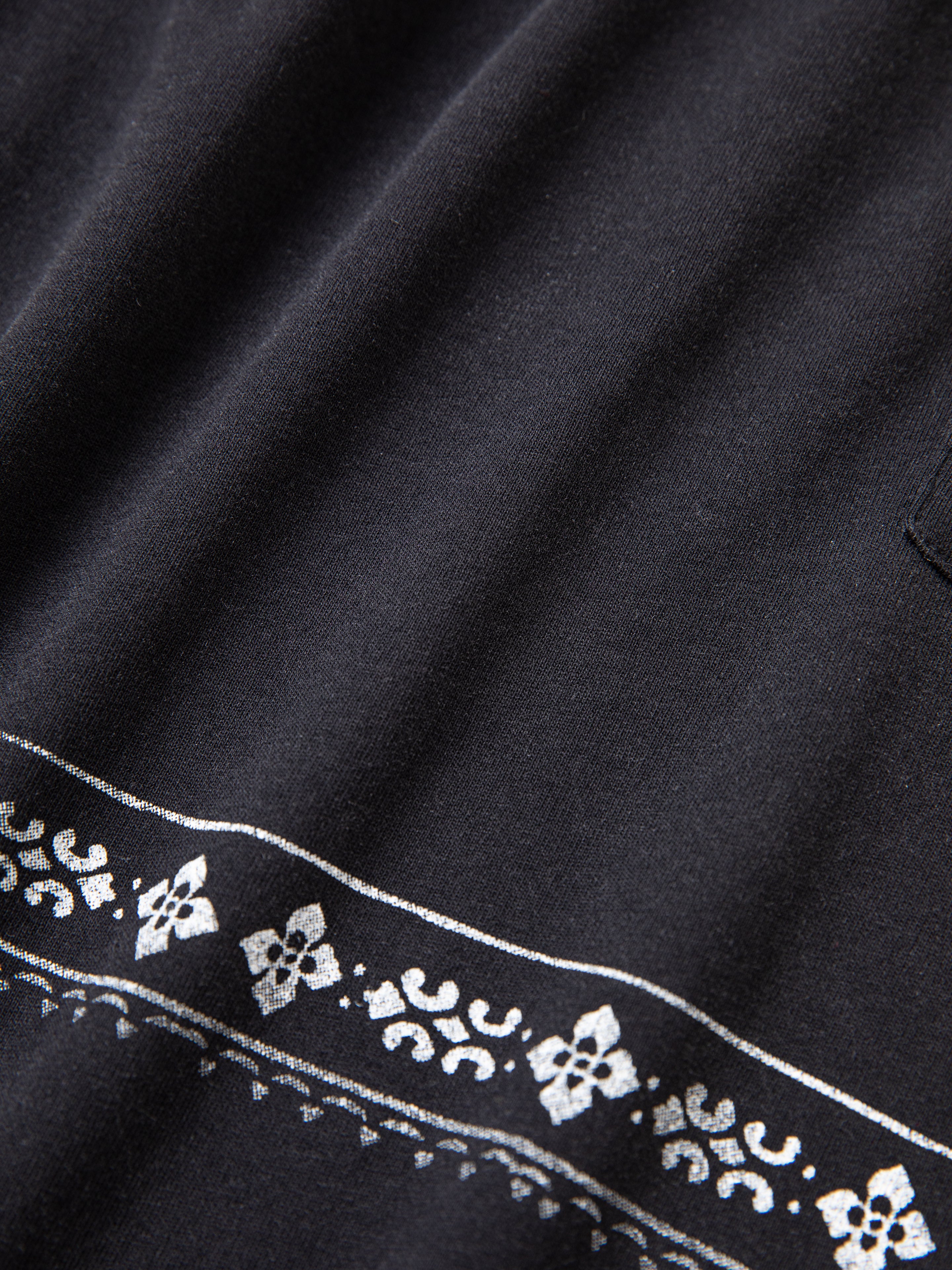 Close-up of the Ornament Pocket Tee by FOUND, showcasing its black fabric with a white floral and geometric border pattern.