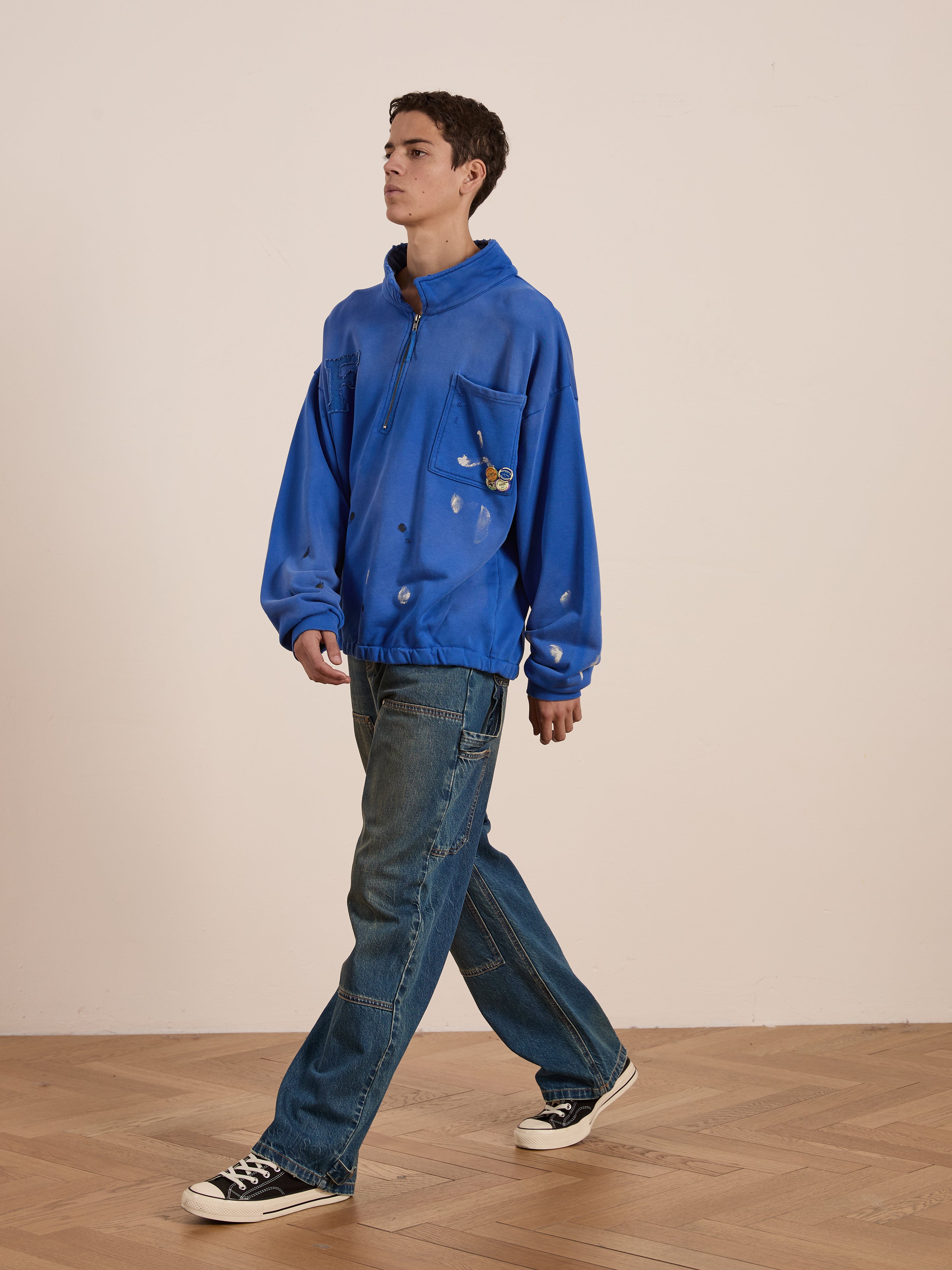 Indoors on a wooden floor, someone in the FOUND Painters Pullover Sweatshirt and jeans exudes relaxed style. The neutral backdrop highlights the unisex workwear's casual appeal.