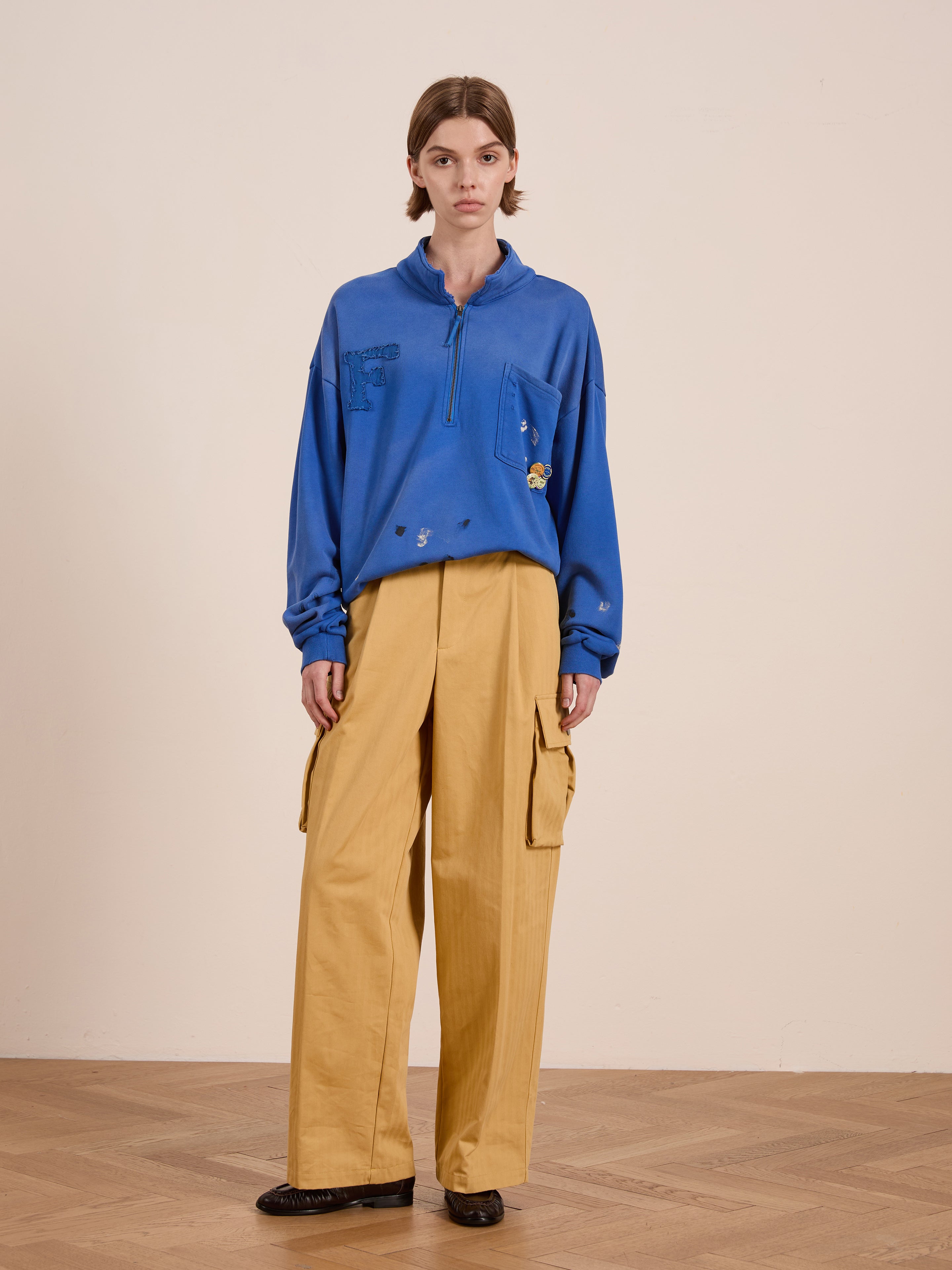 A person in a FOUND Painters Pullover Sweatshirt and yellow cargo pants stands on a wooden floor against a plain wall, highlighting ideal unisex workwear style.