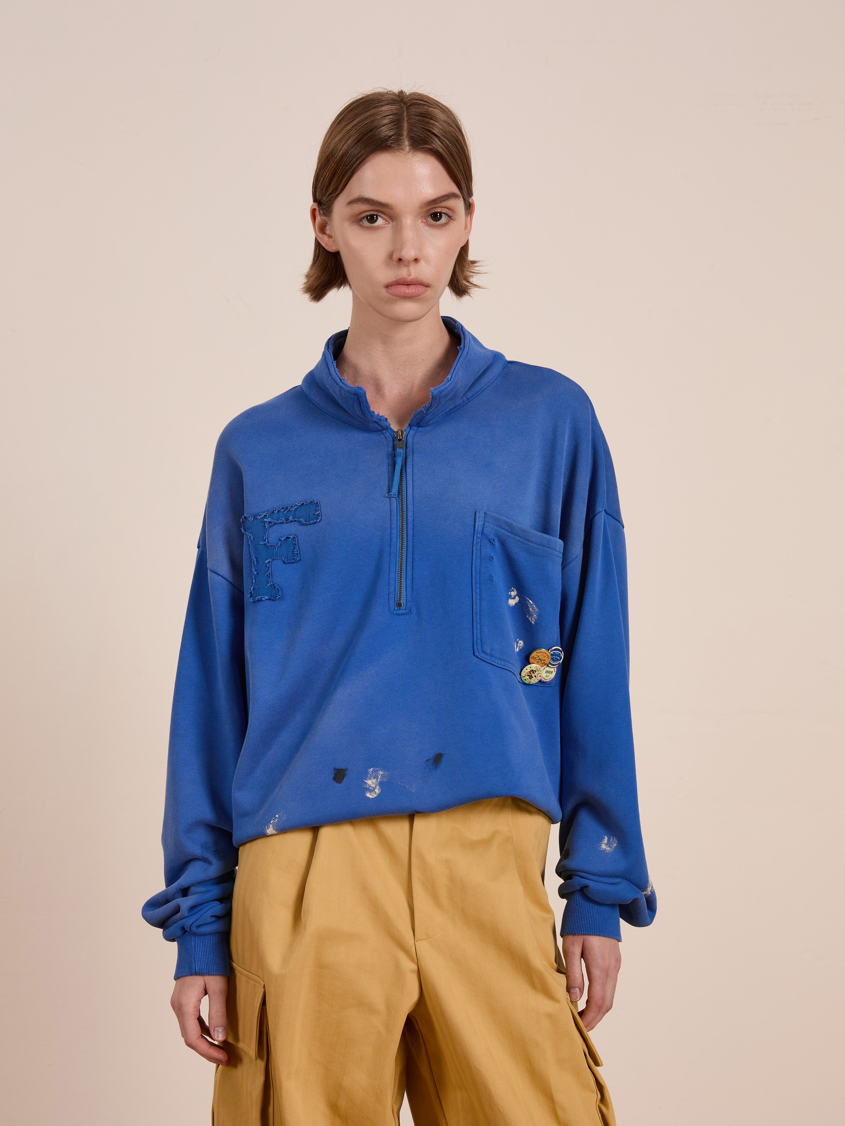 A person in a blue FOUND Painters Pullover Sweatshirt pairs it effortlessly with tan pants, standing against a plain background.