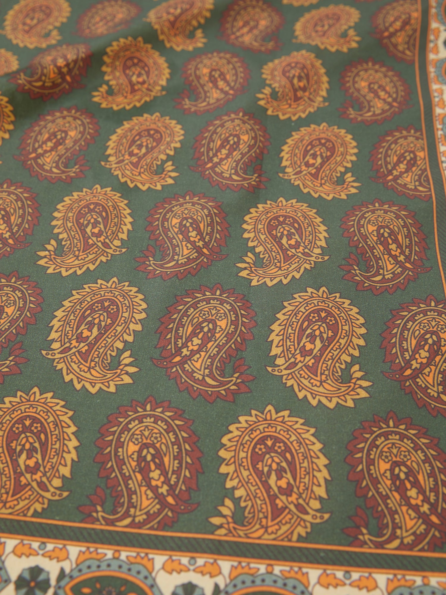 A Paisley Forest Bandana by Found in a cotton blend fabric with green and orange colors.
