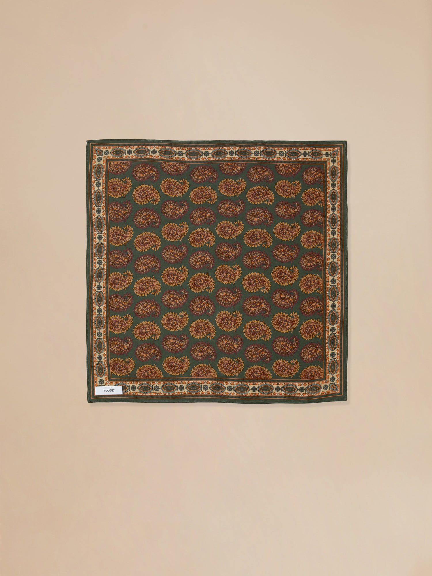 A brown and orange Coming Soon | Paisley Forest Bandana hanging on a beige wall, found by Found.