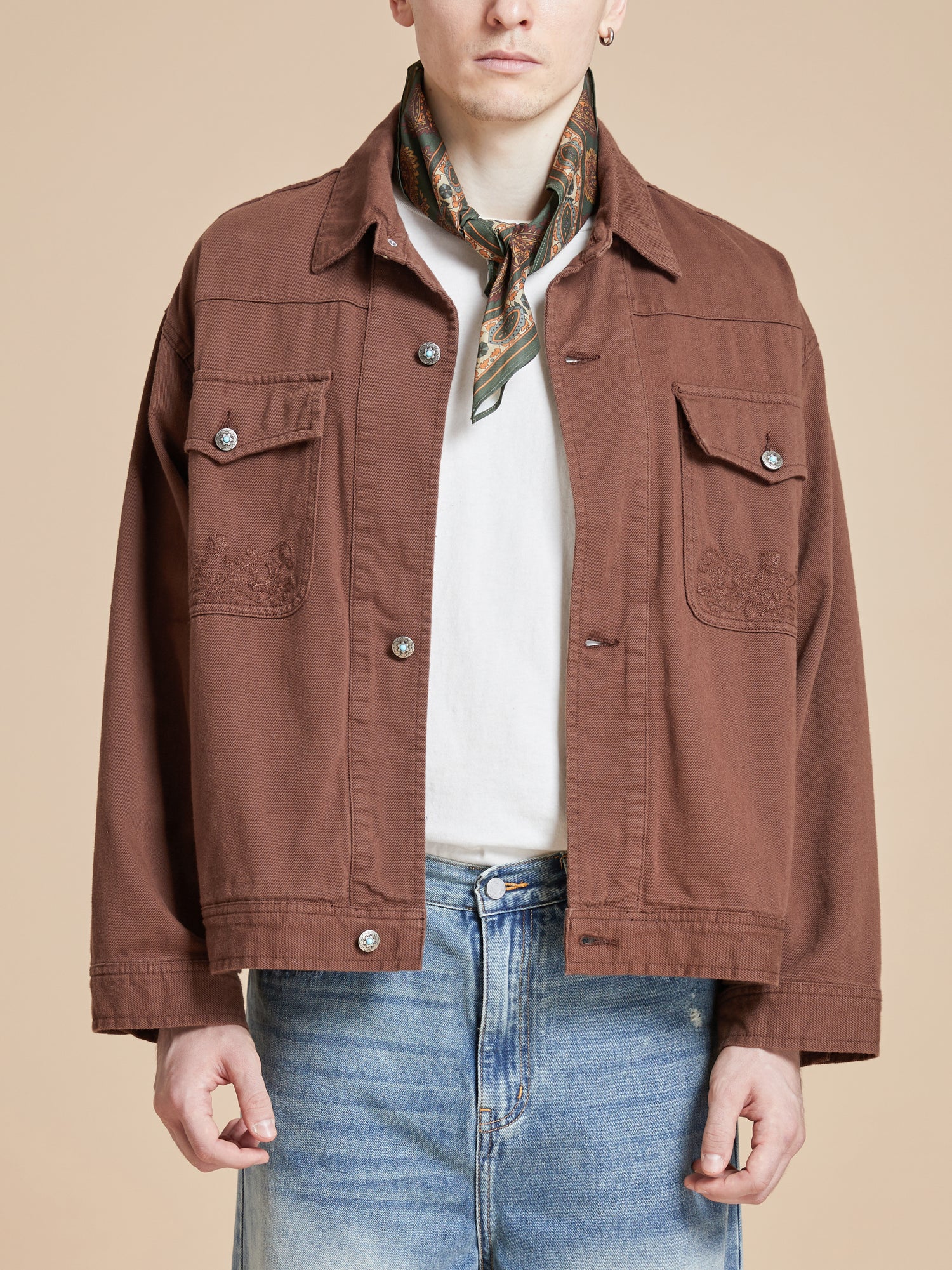 A man wearing a brown jacket and jeans featuring Found Paisley Forest Bandana.