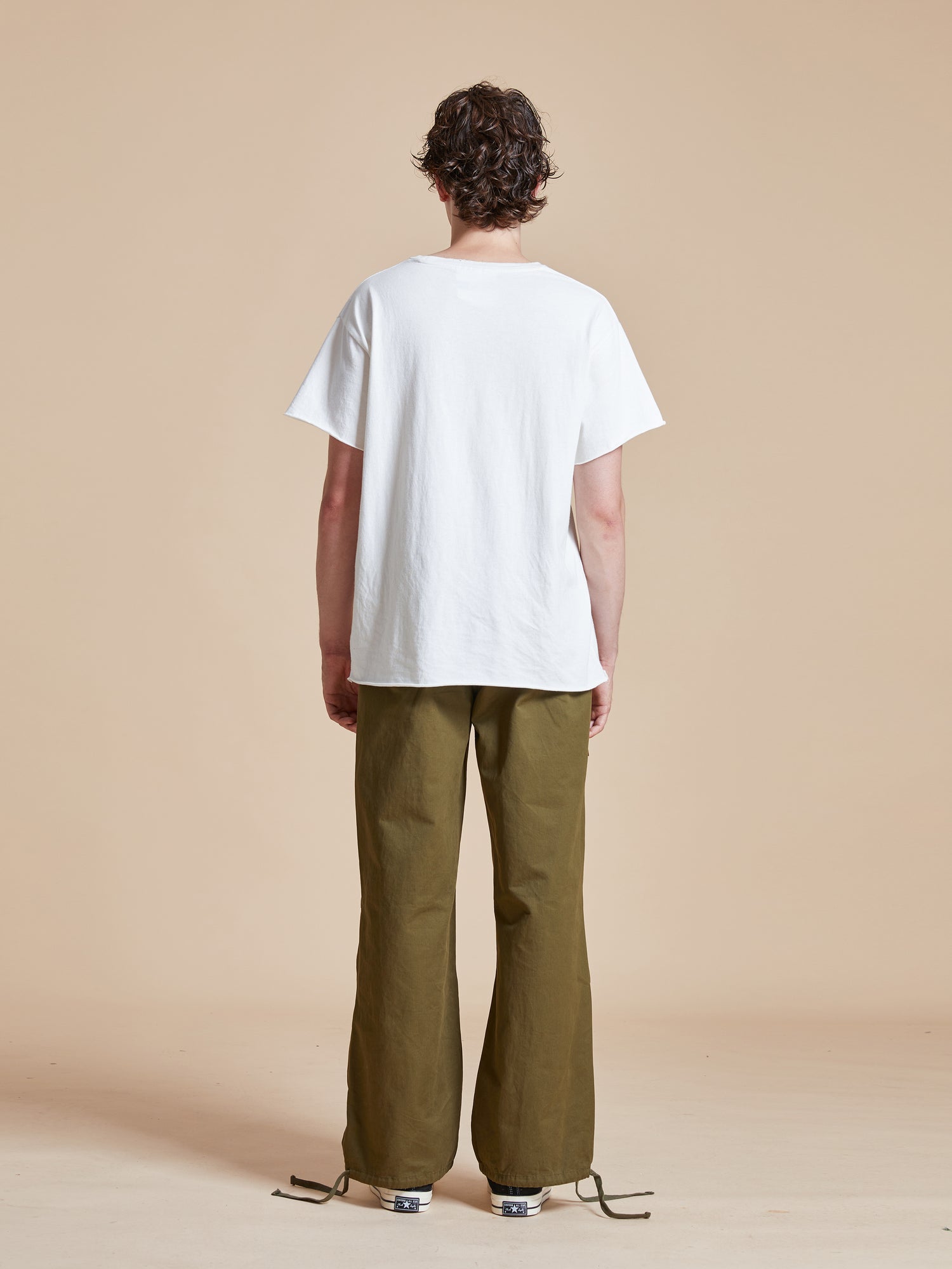 The back view of a man wearing a white t-shirt and Found Parachute Cargo Twill Pants.