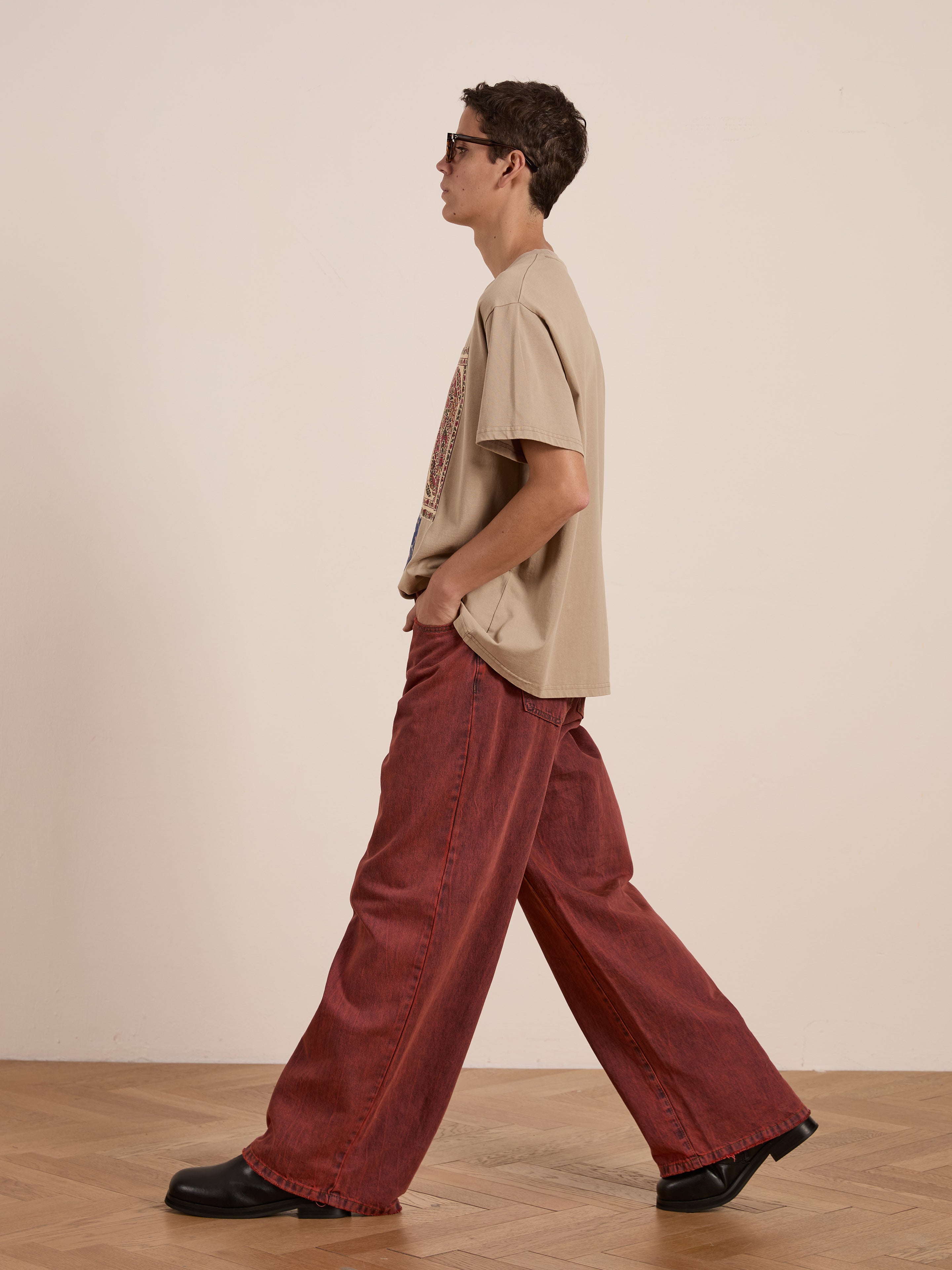 A person wearing FOUND's Patchwork Tee with subtle Kantha embroidery, red wide-leg pants, sunglasses, and black shoes walks on a wooden floor against a plain background.