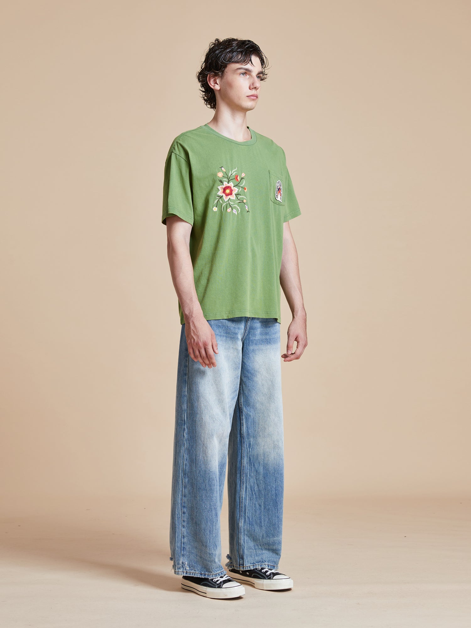 A man wearing a Pine Needle Farm Tee by Found and blue jeans.
