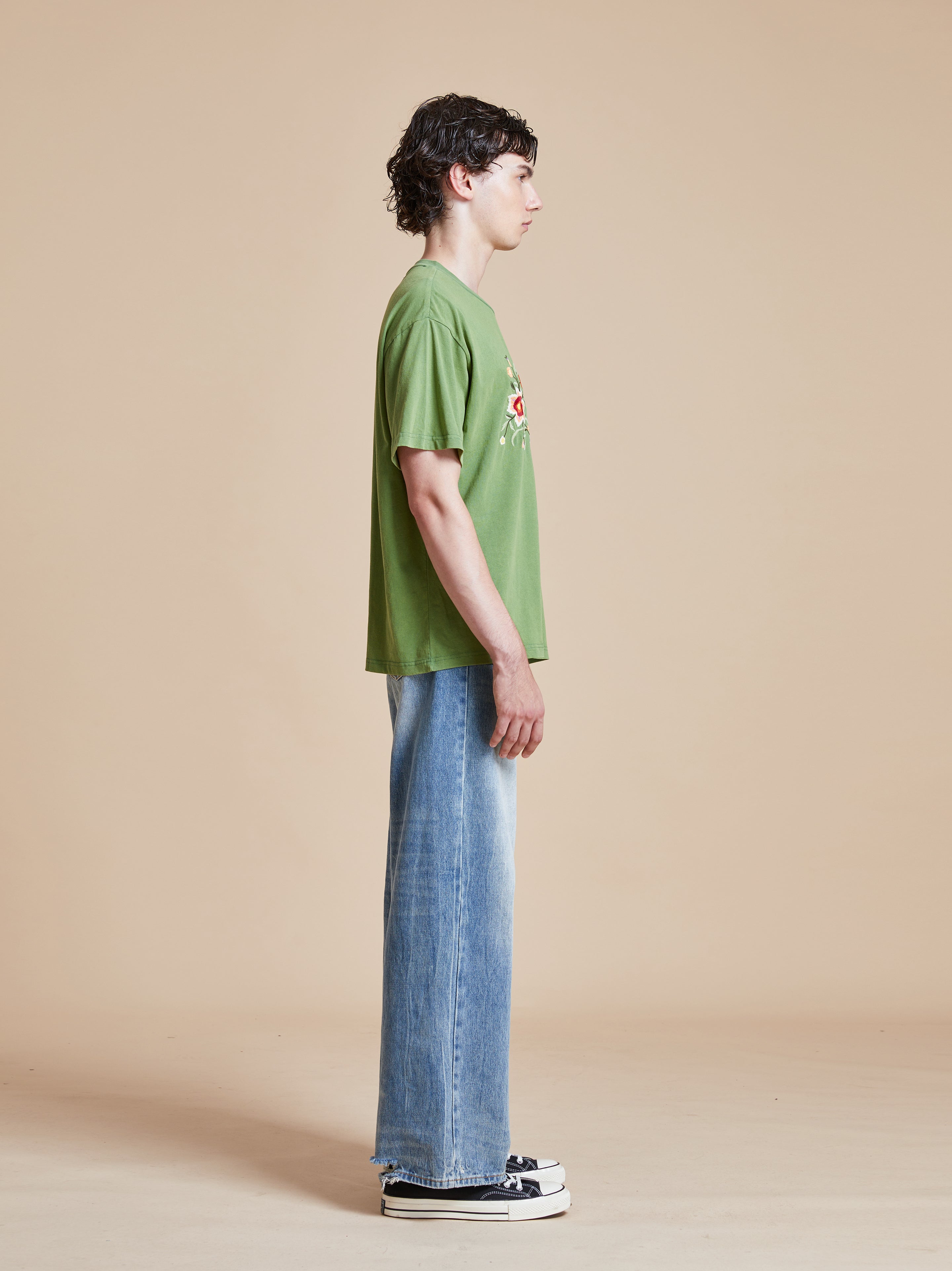 A man wearing a Pine Needle Farm Tee by Found and blue jeans.