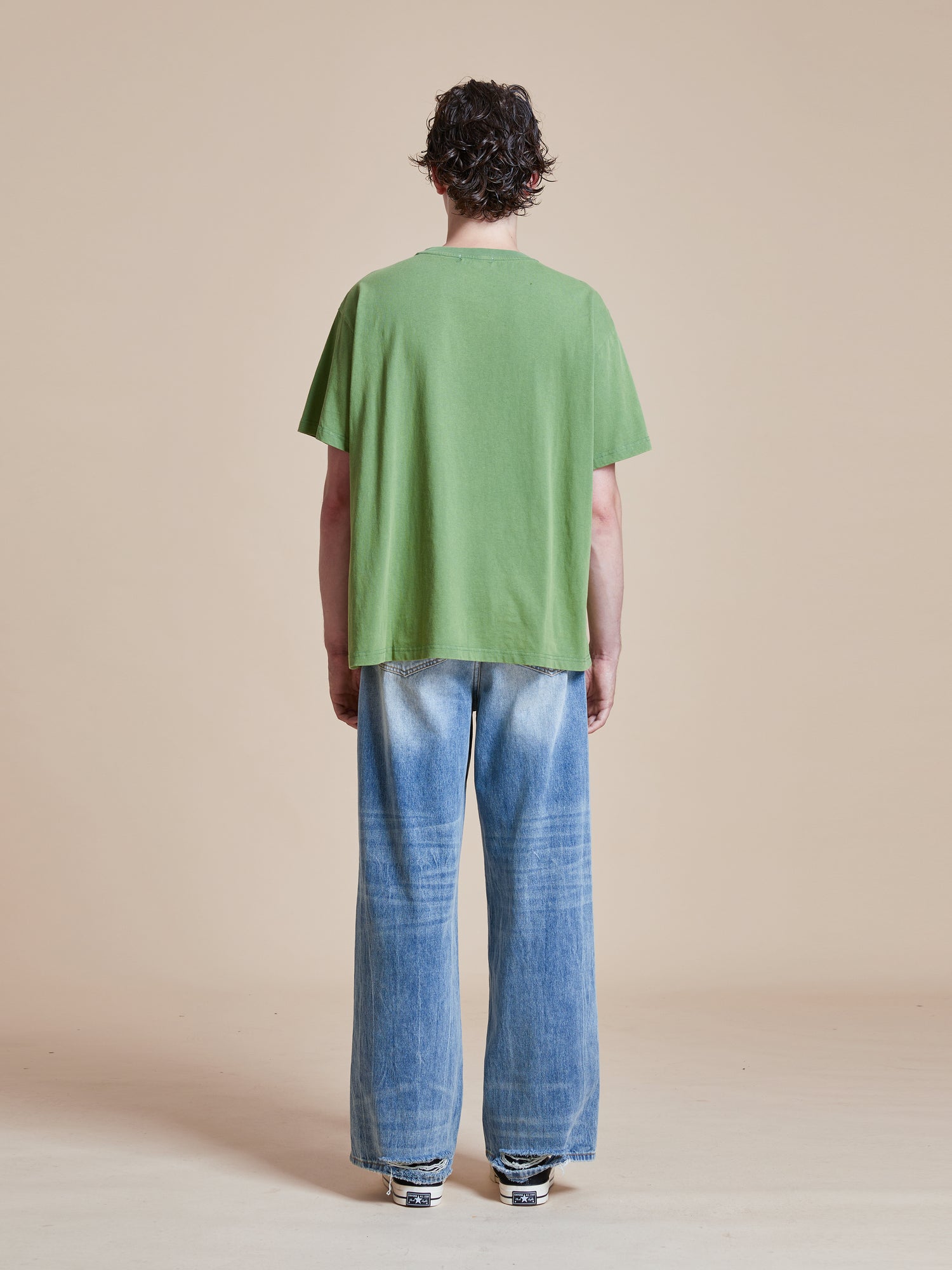 The back view of a man wearing a Pine Needle Farm Tee by Found and blue jeans.
