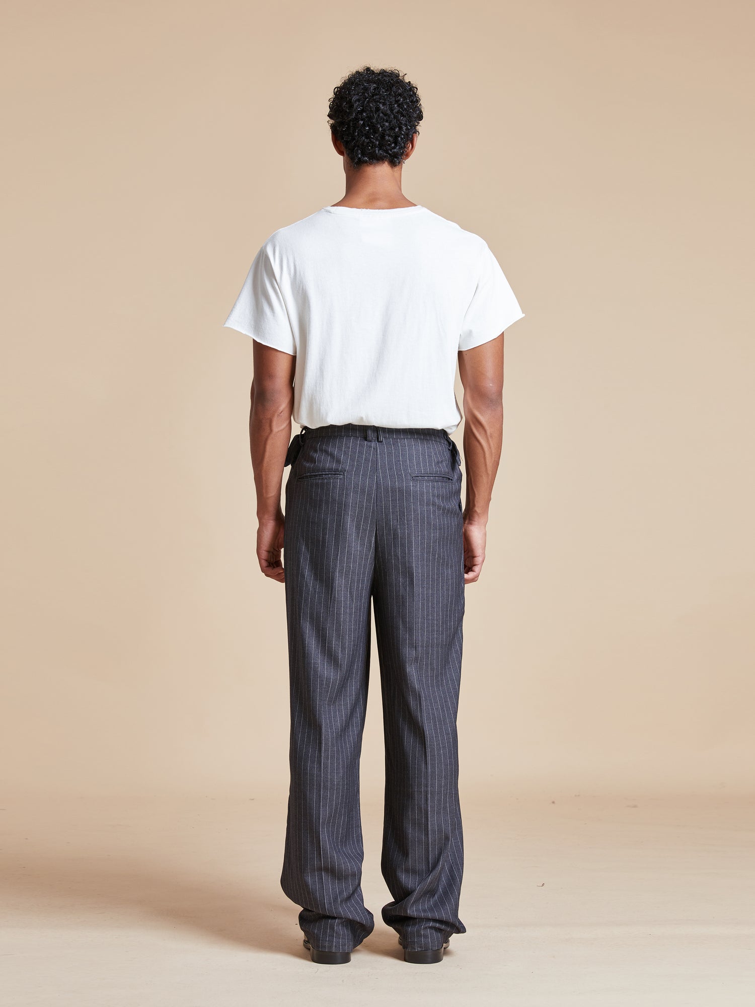 The back view of a man wearing a white t-shirt and Found Pinstripe Pleated Trousers.