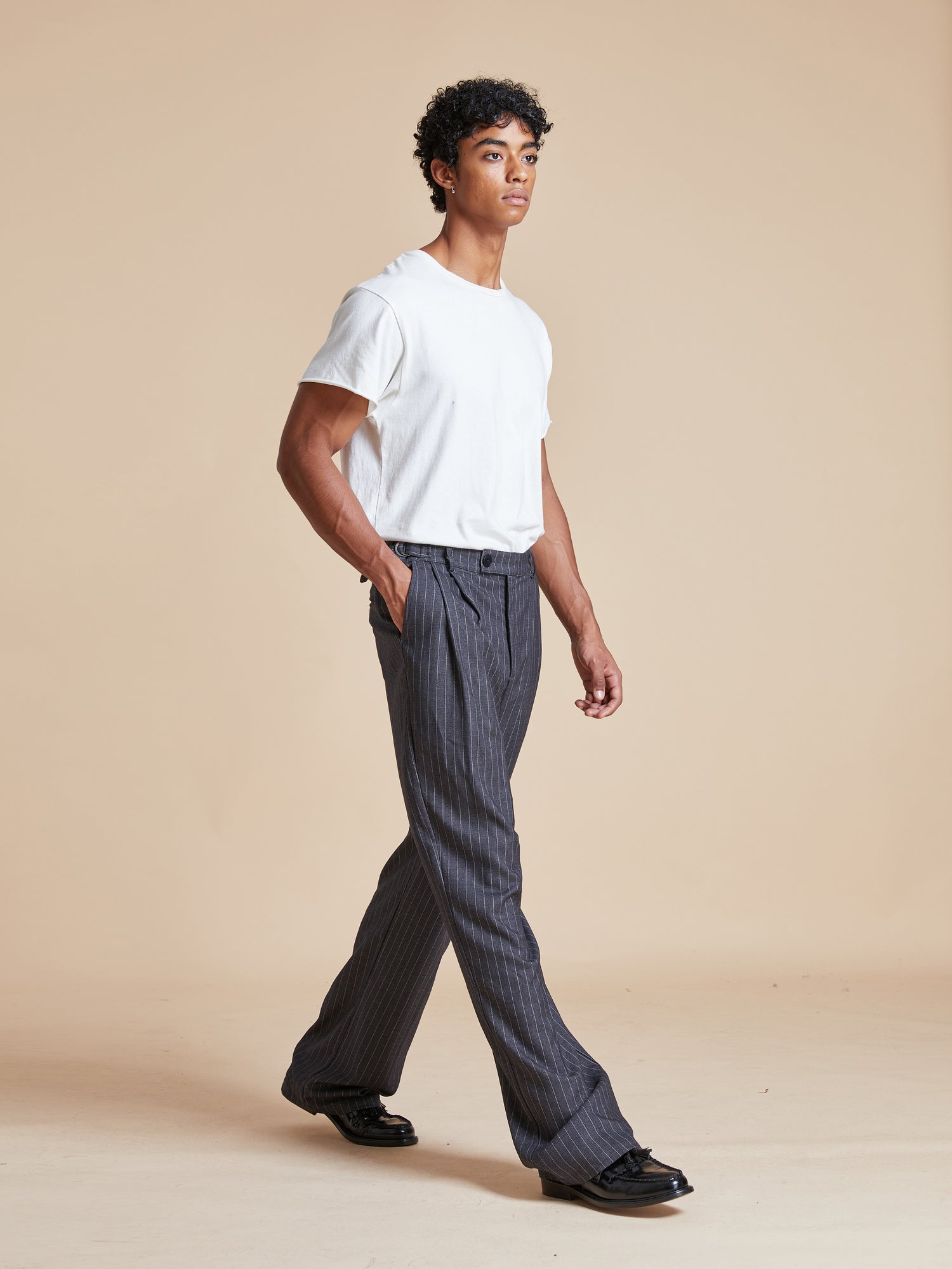 The model is wearing a white t-shirt and Found Pinstripe Pleated Trousers.