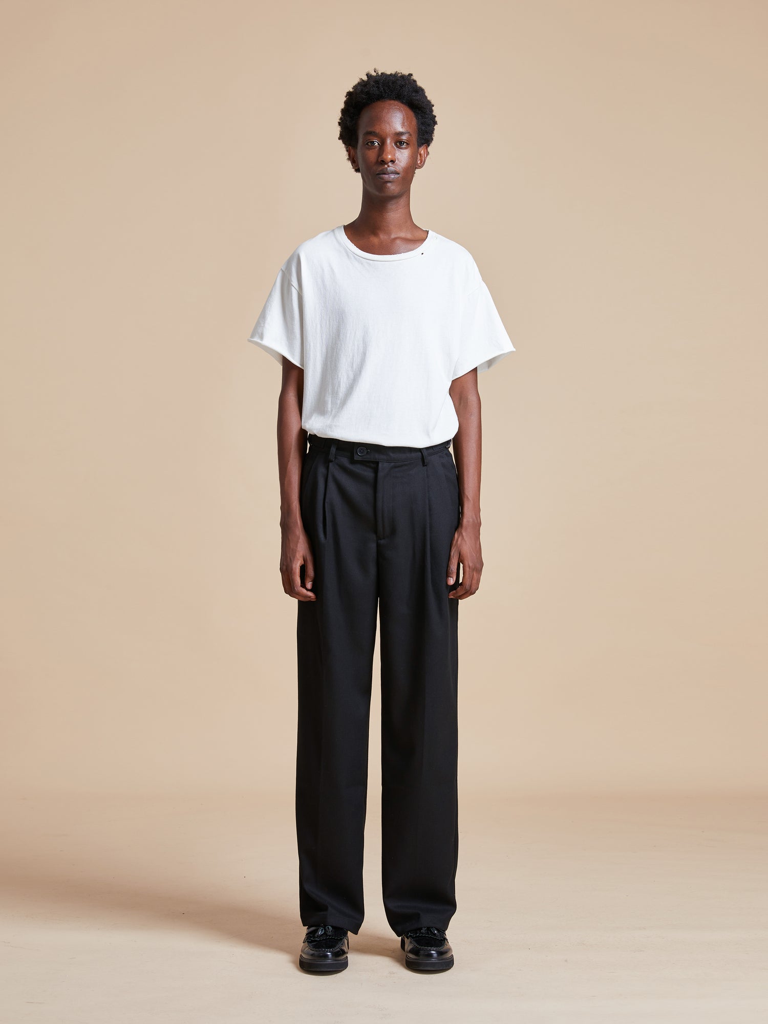 The model is wearing a white t-shirt and Found Pleated Trousers.