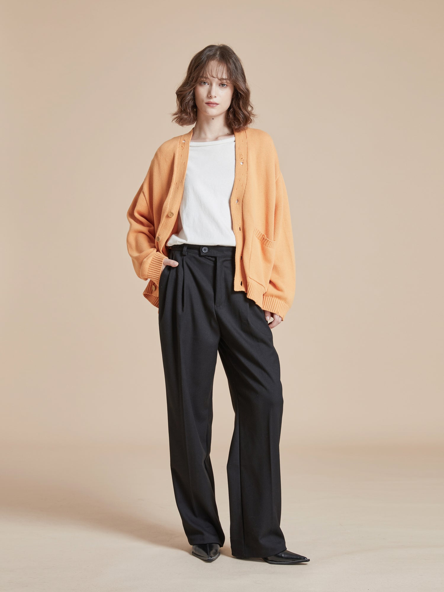 The model is wearing a classic cardigan and black Found Pleated Trousers to create a stylish silhouette.