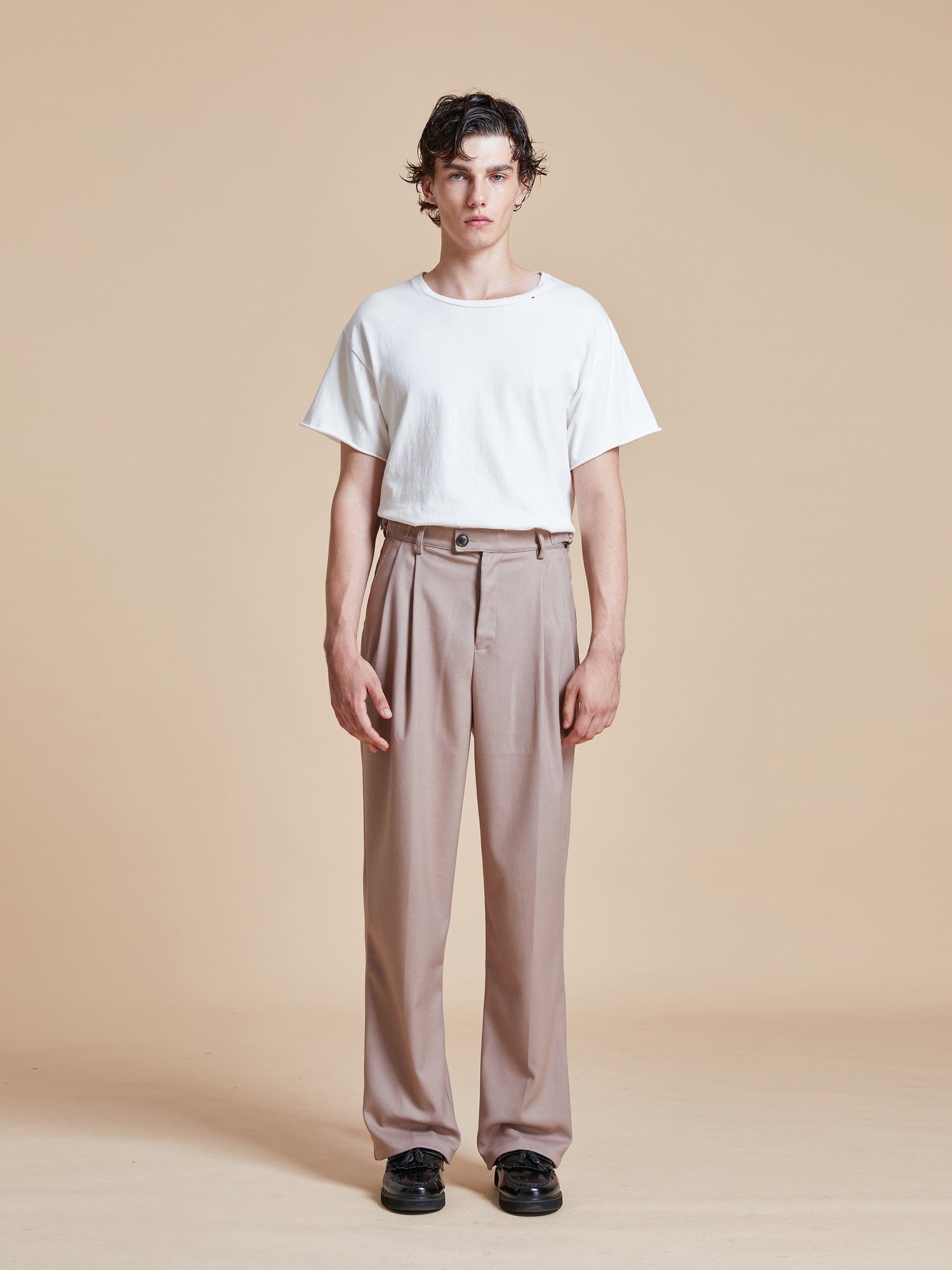 The model is wearing a white t - shirt and Found beige Pleated Trousers.