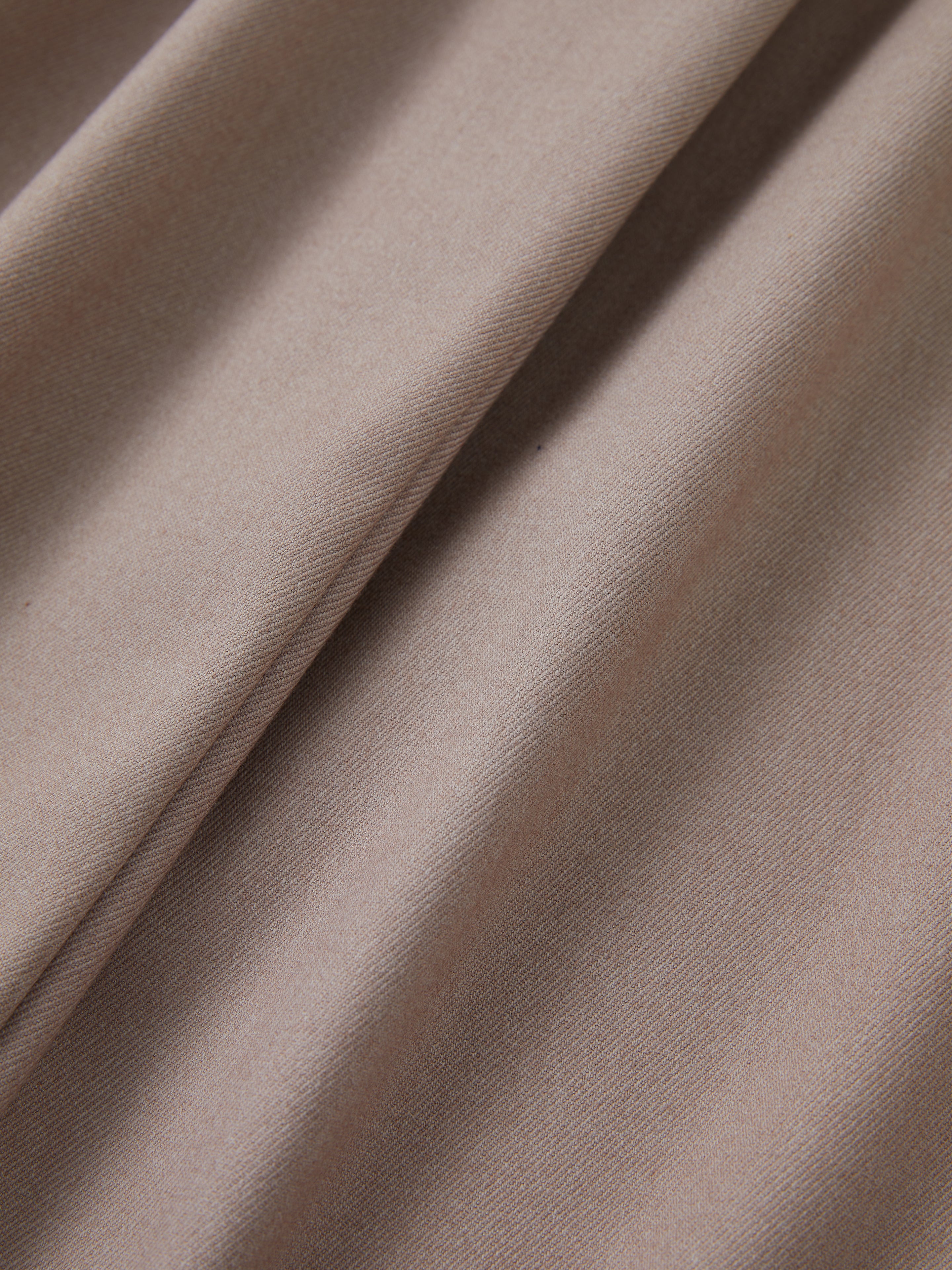 Close-up of folded light brown fabric displaying its soft and smooth texture, perfect for those Found Pleated Trousers with adjustable waist tabs.