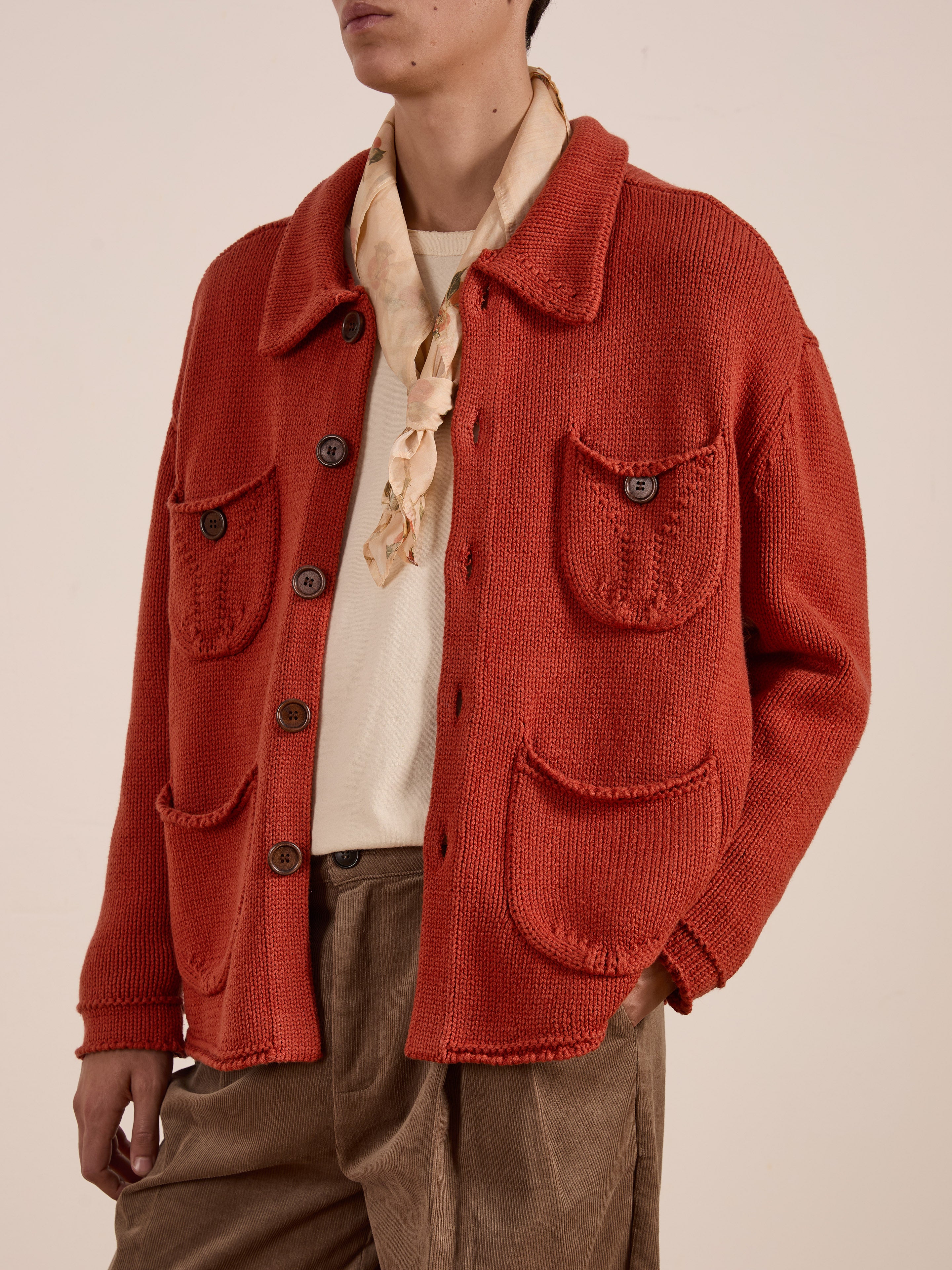 A person is wearing FOUND's Hunter Knit Collared Cardigan in red, layered over a white shirt. They have a beige scarf around their neck and brown pants, creating an ideal transitional look for in-between seasons.