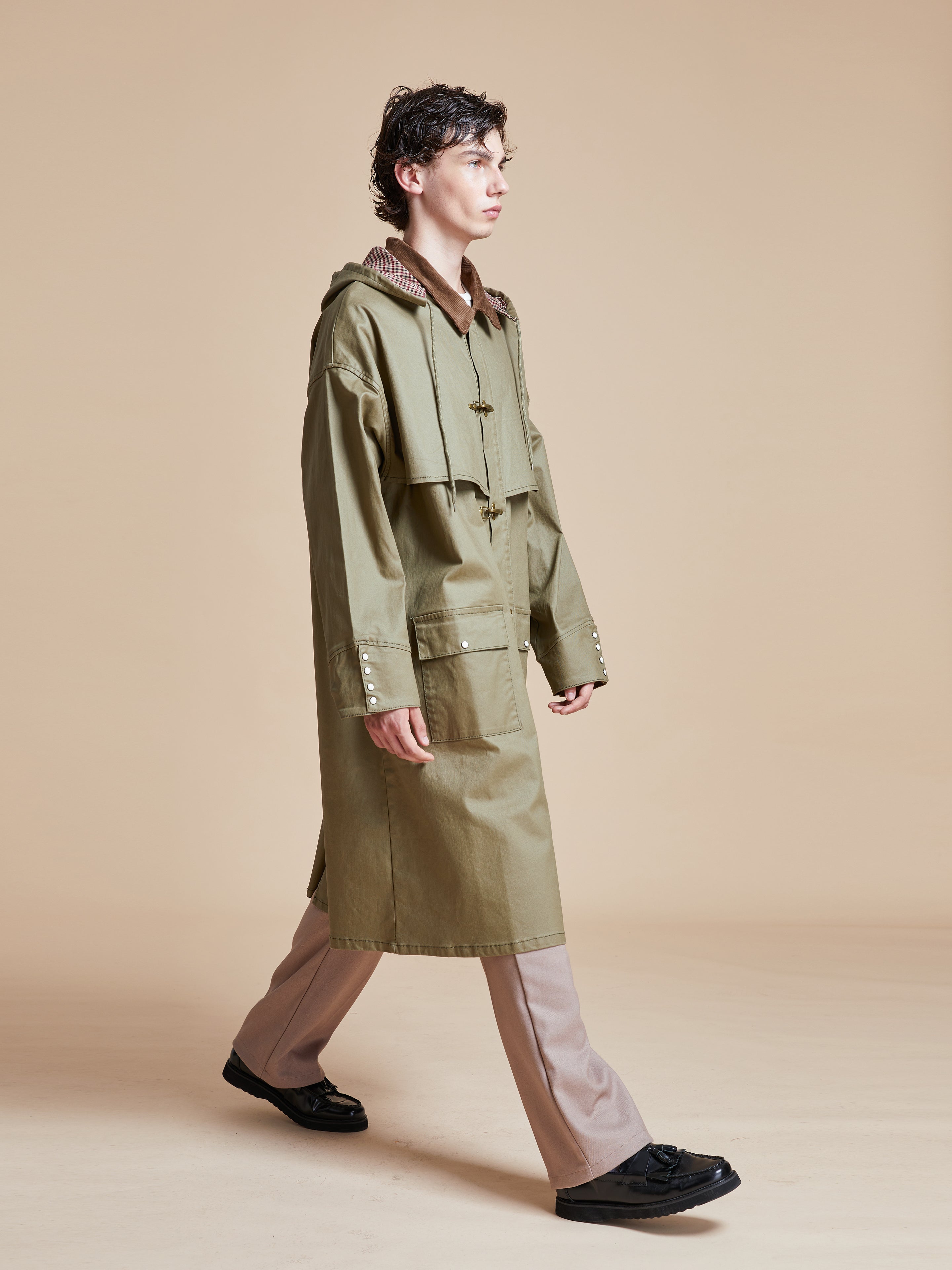 A man in a Found Prairie Buckle Coat walking on a beige background.