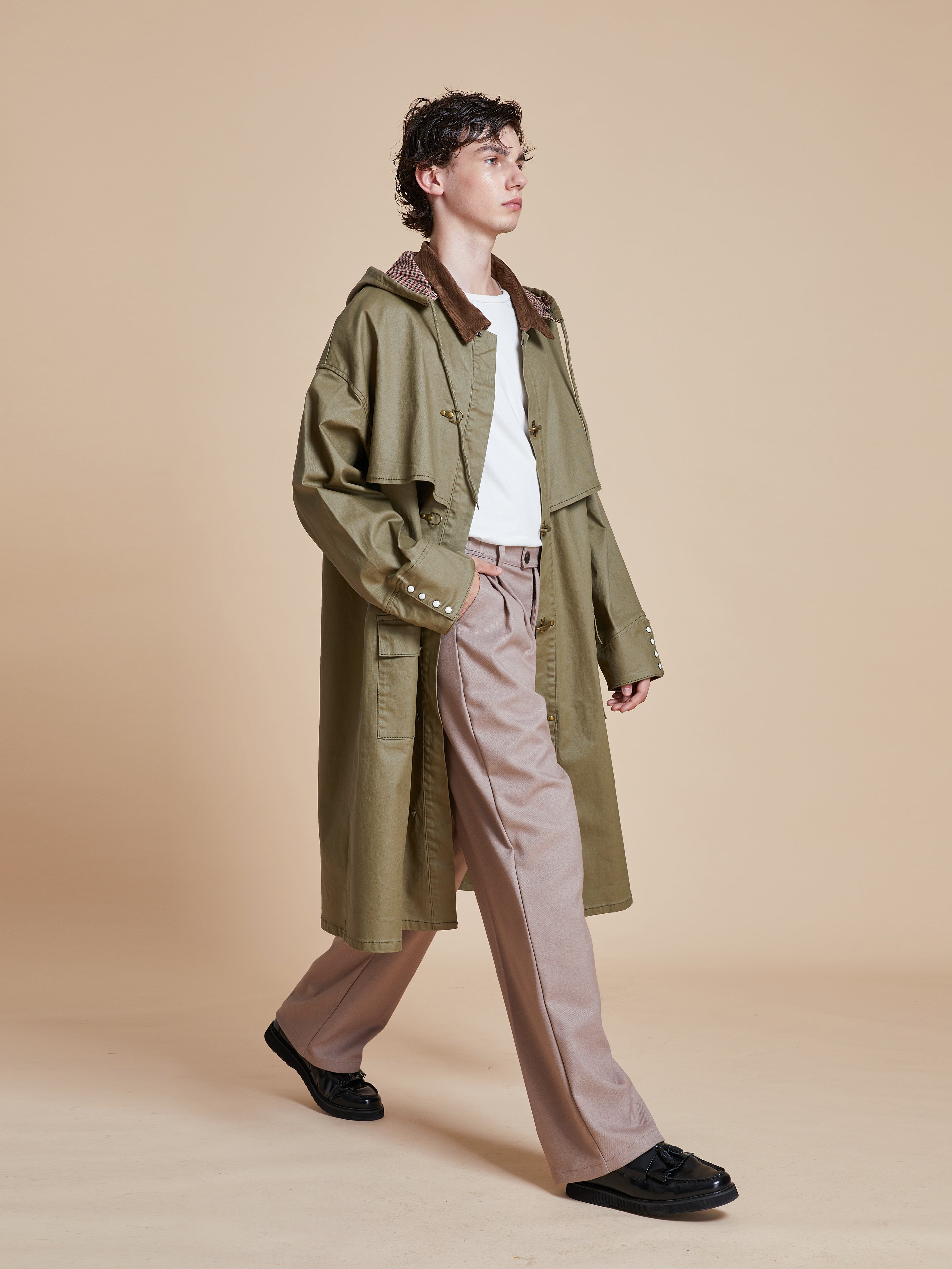 A man in a Found Prairie Buckle Coat walking on a beige background.