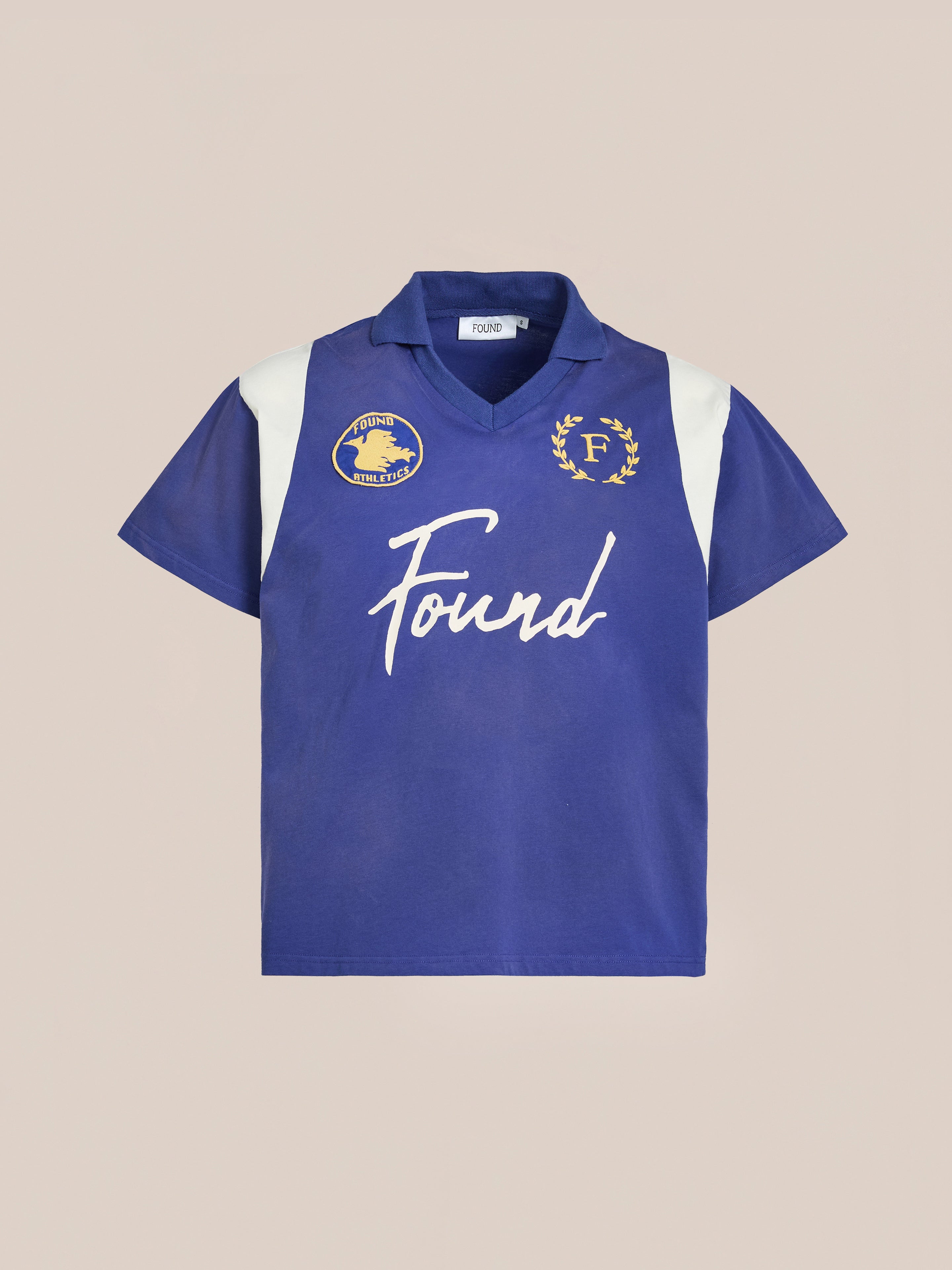 Premier League Jersey by FOUND: A blue short-sleeve polo with white accents and embroidered crest, featuring chest emblems and "Found" across the front, capturing the vintage sportswear's timeless appeal.