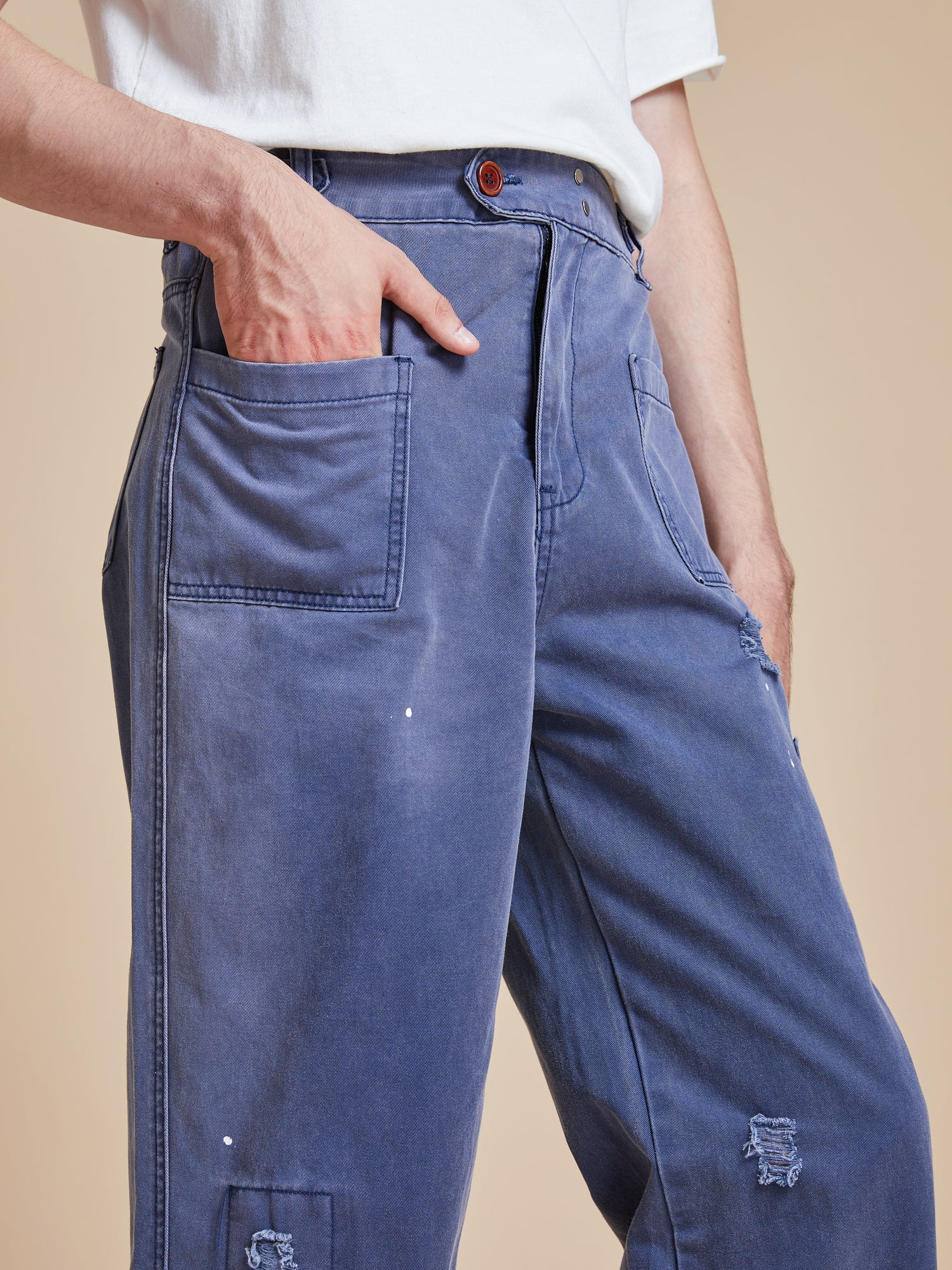 A man is wearing Found River Painters Chore Pants with holes in them.