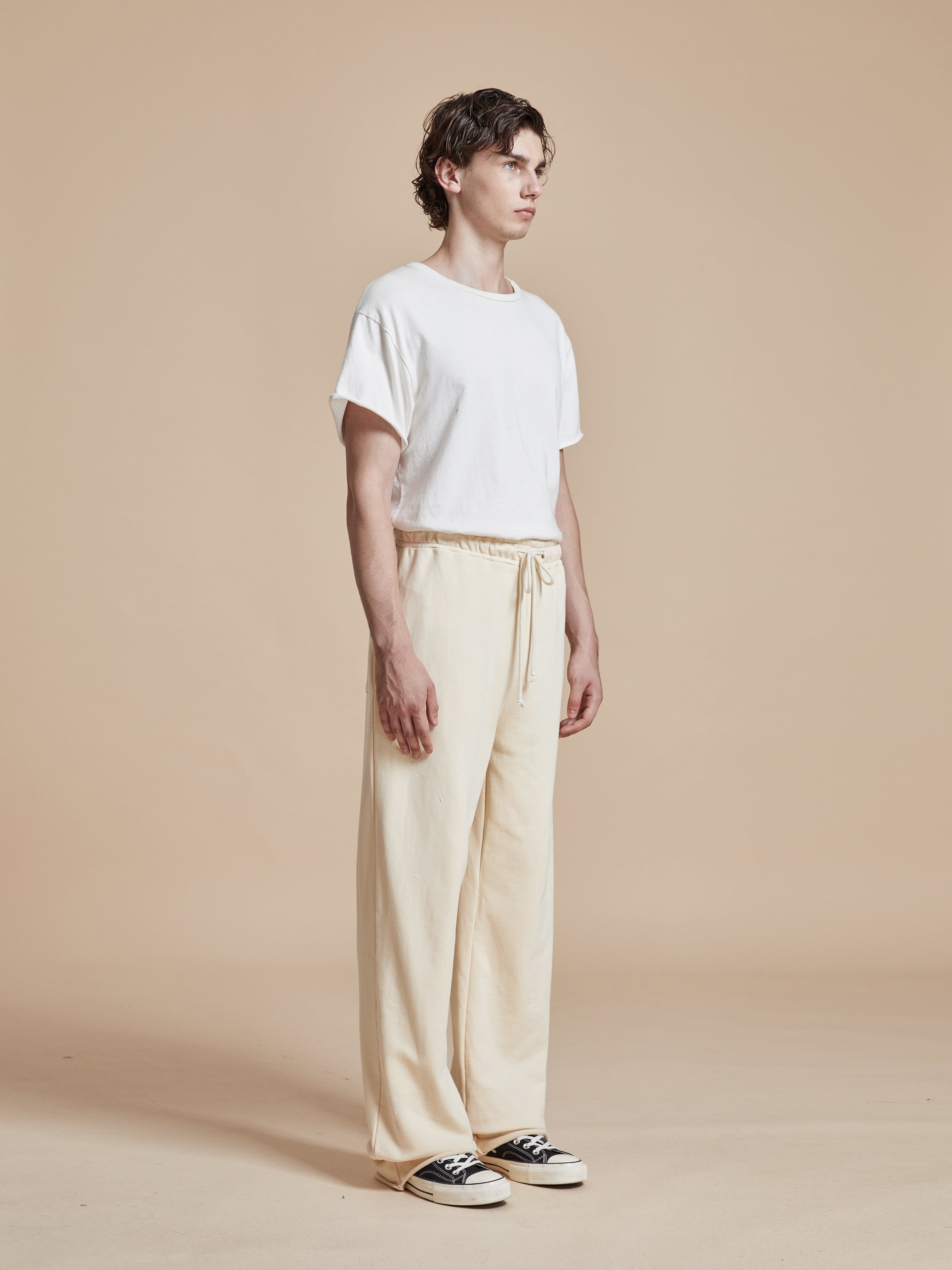 The model is wearing a white t-shirt and beige Found Sandshell Lounge Pants - both wardrobe staples.