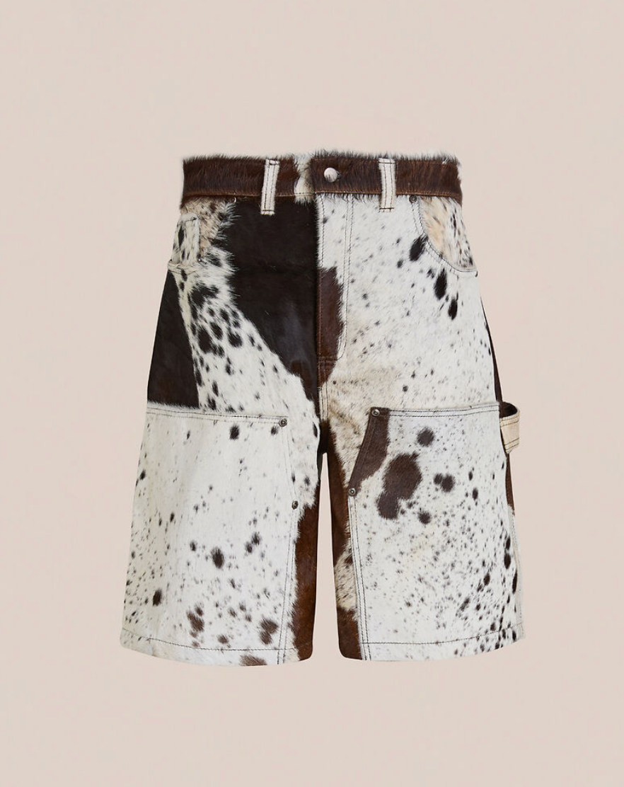 The Found Cowhide Prairie Carpenter Shorts are unisex, relaxed fit cargo shorts crafted from genuine cowhide leather with a white, brown, and black spotted pattern, displayed against a plain beige background.