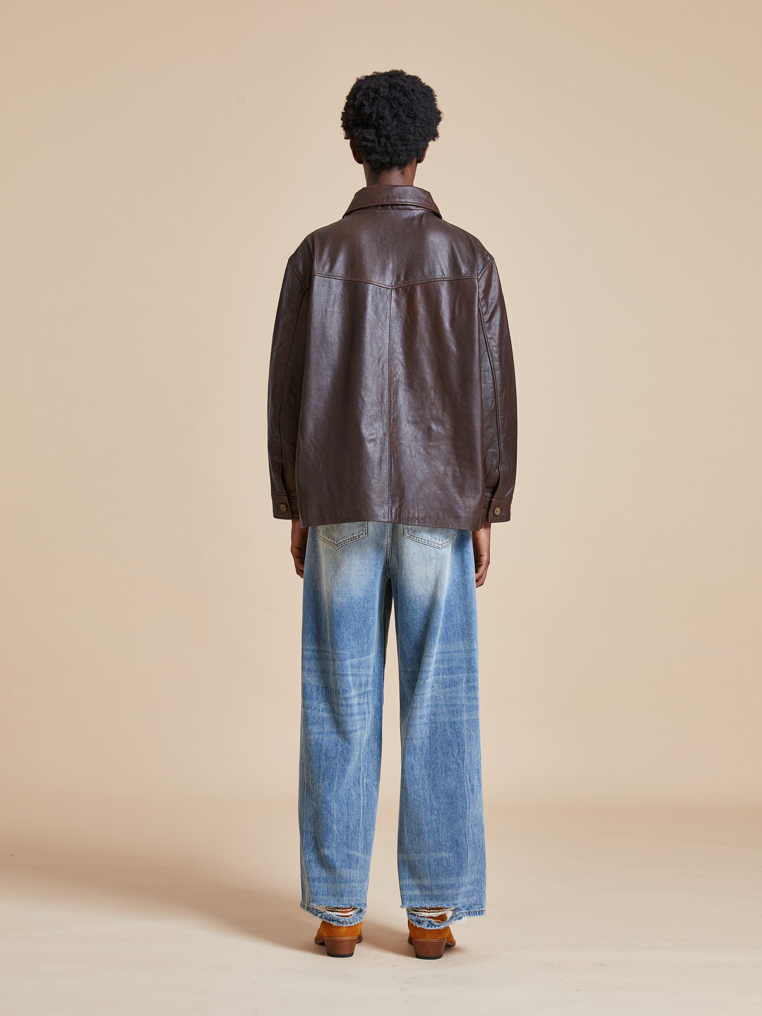 The back view of a man wearing a Found Sepia Leather Overshirt and jeans.