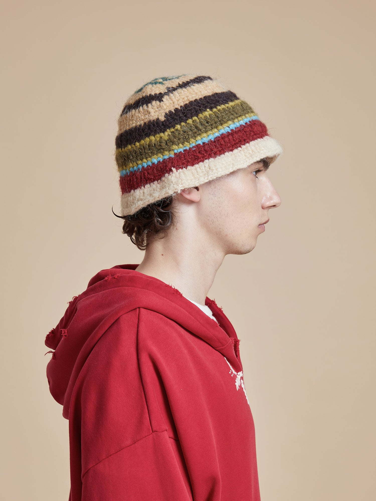 A man wearing a red hoodie with a Found Stripe Knit Beanie hat.