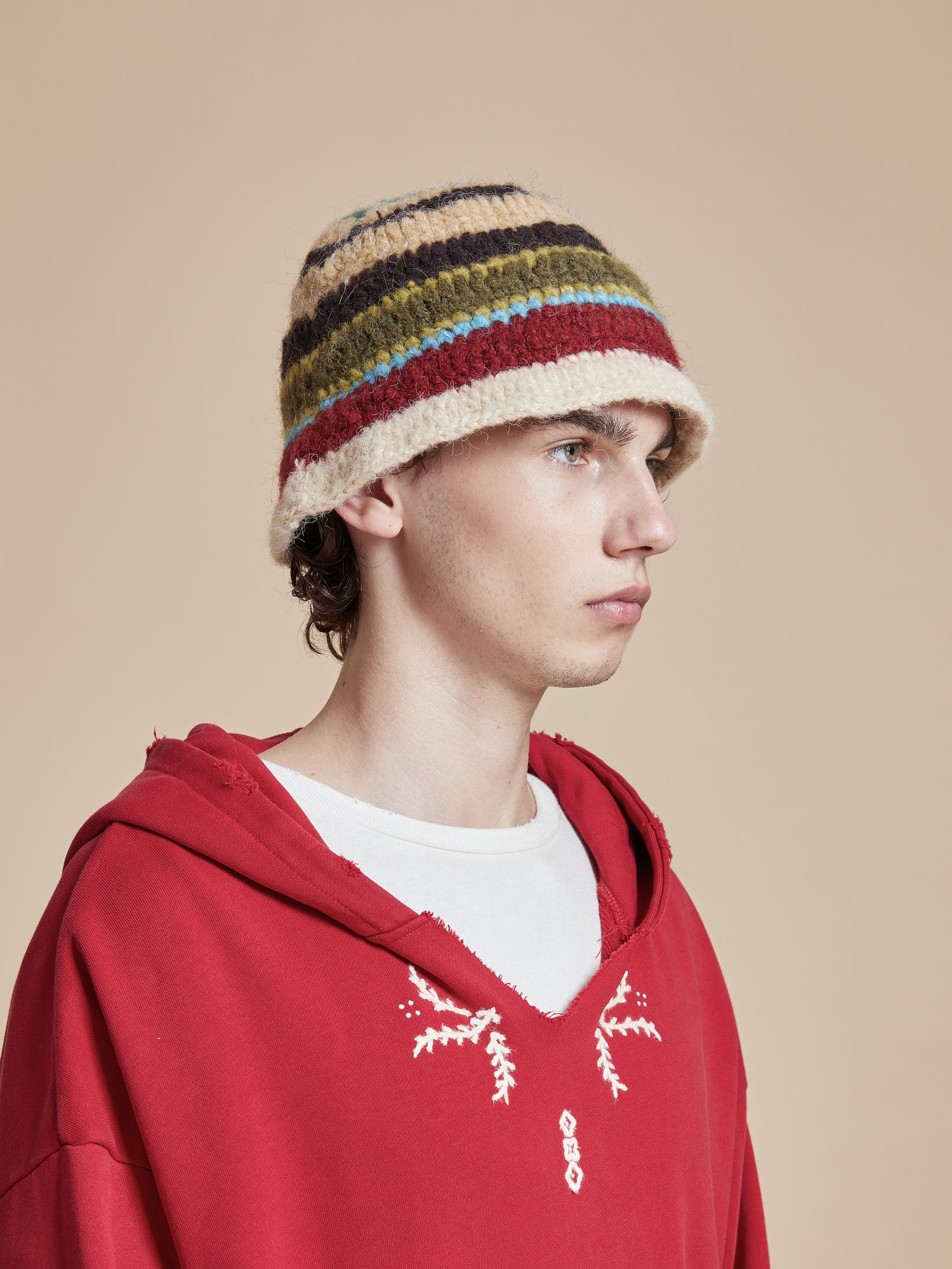 A young man wearing a red hoodie with a striped hat featuring a Found Stripe Knit Beanie.