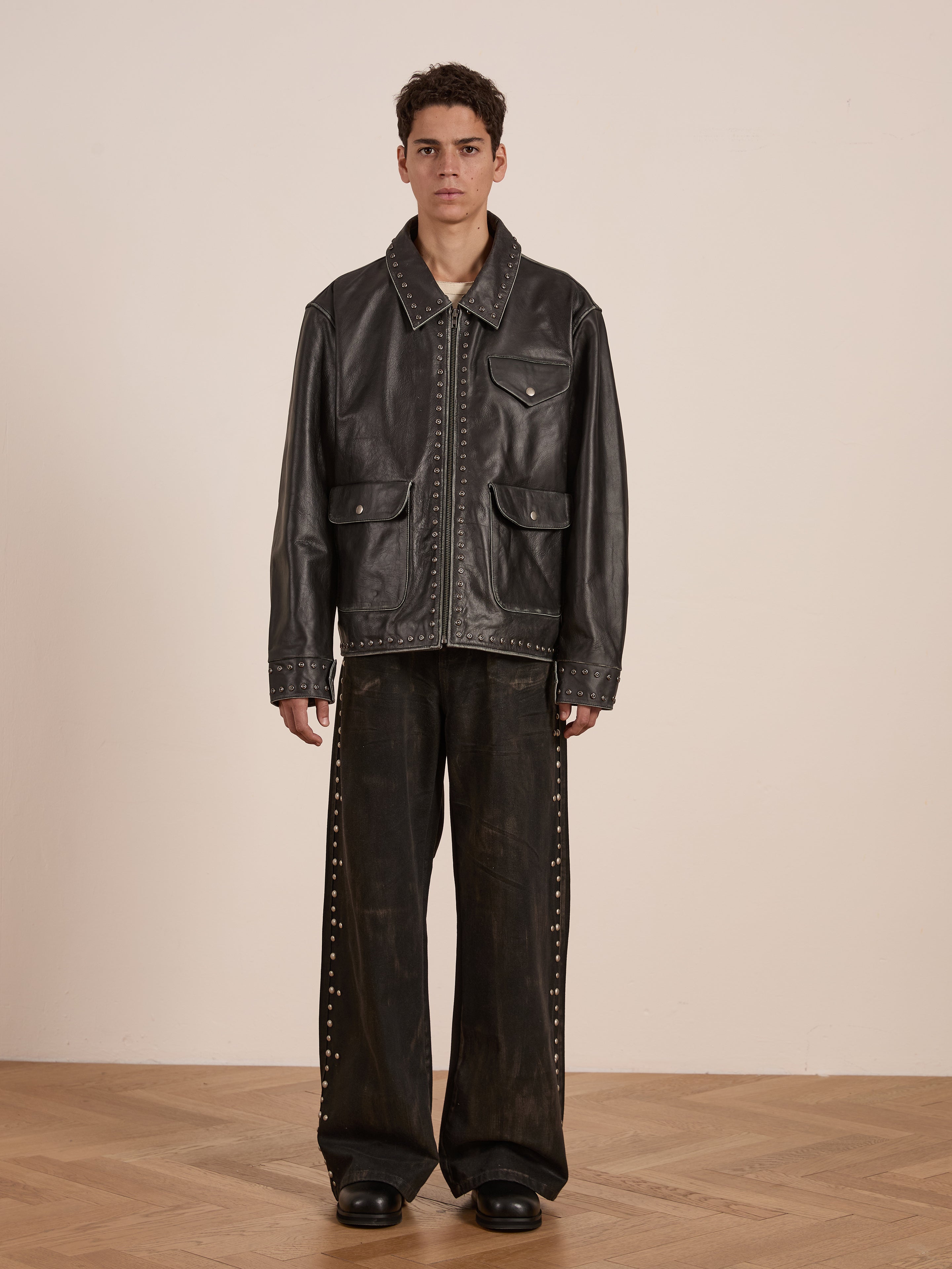 A person wearing the Found Studded Leather Pocket Jacket and wide-leg pants with stud details stands on a wooden floor against a plain backdrop.