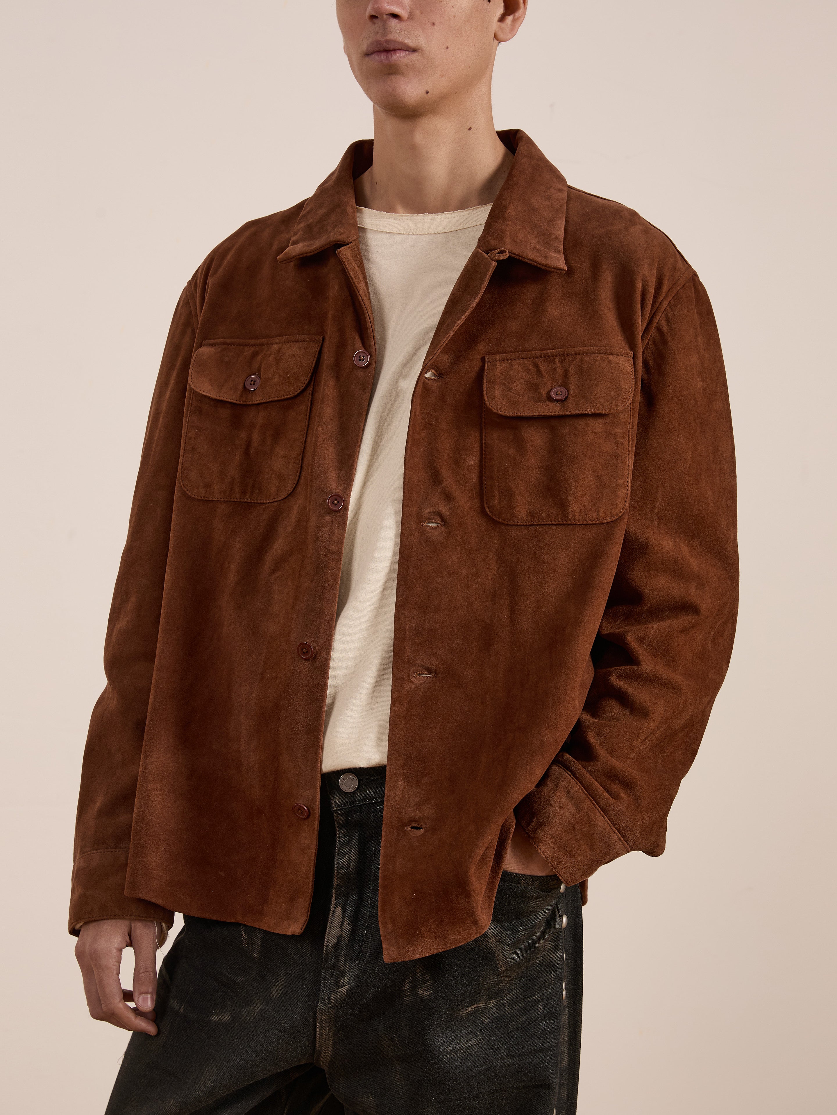 Someone is styled in the FOUND Suede Camp Shirt, a genuine goat suede leather jacket with buttoned pockets, over a beige shirt and dark pants for a relaxed silhouette.