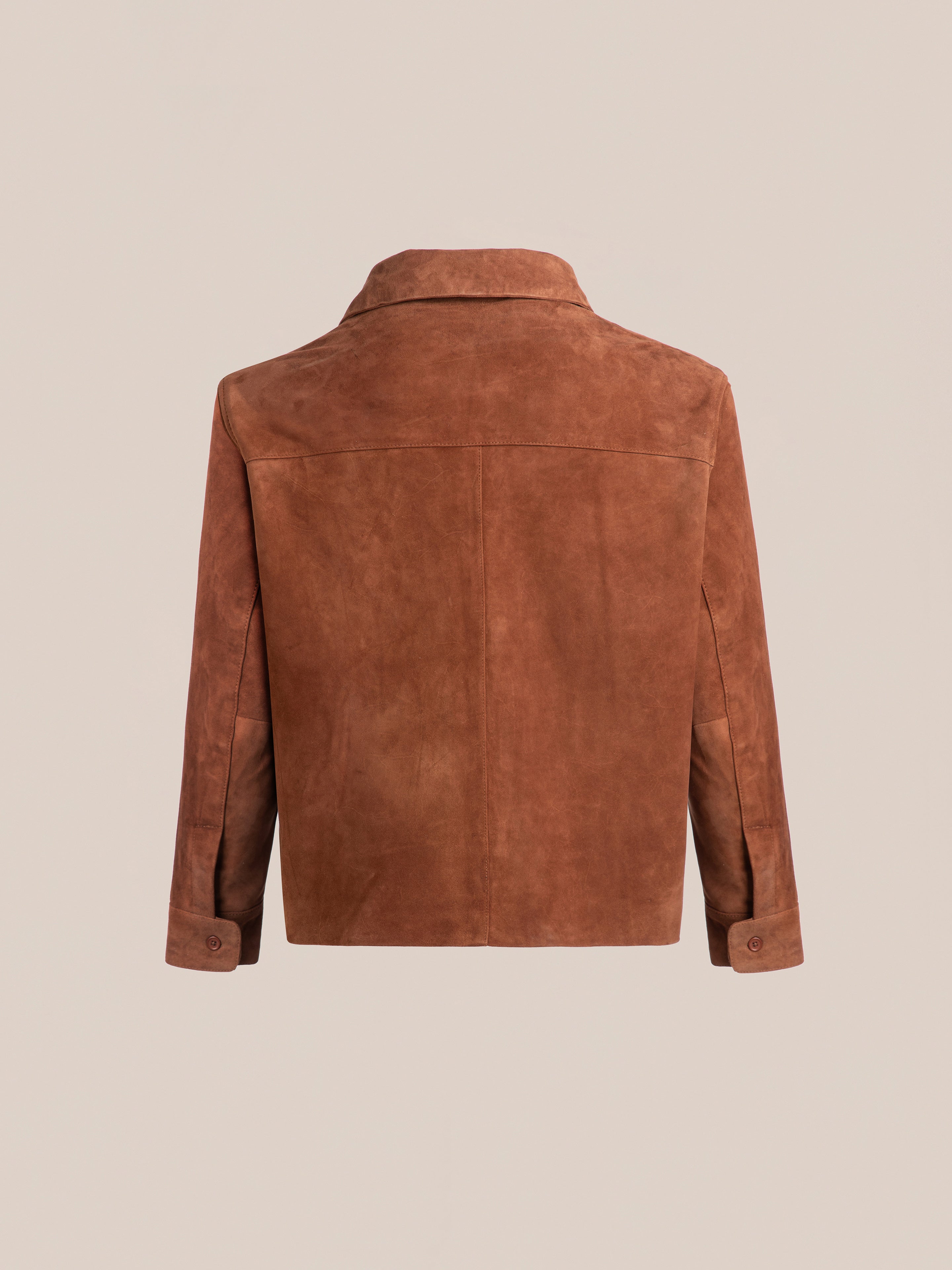 The Suede Camp Shirt by FOUND is a brown jacket made from genuine goat suede leather, featuring a back view with a wide collar and buttoned cuffs. Its relaxed silhouette is inspired by the classic design.