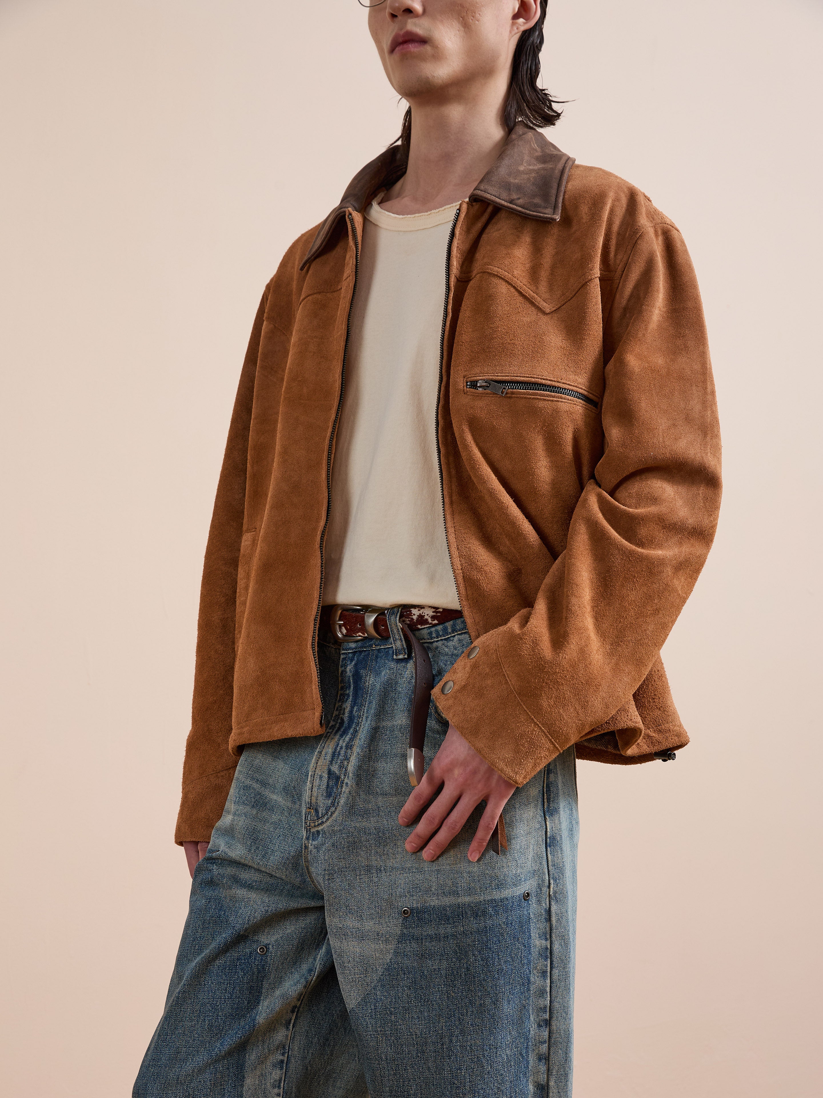 A person wears the FOUND Suede Western Barn Jacket over a beige t-shirt and faded blue jeans, standing against a plain, light-colored background.