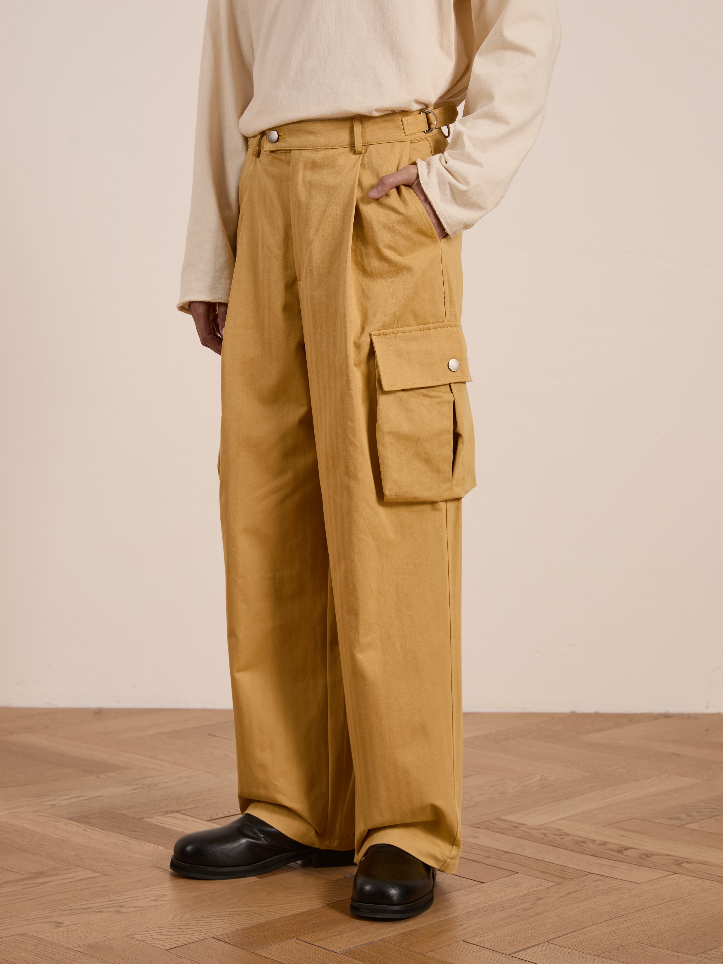 A person stands on a wooden floor wearing FOUND's Sunlight Twill Cargo Pants in a striking mustard color, paired with a beige long-sleeve shirt.