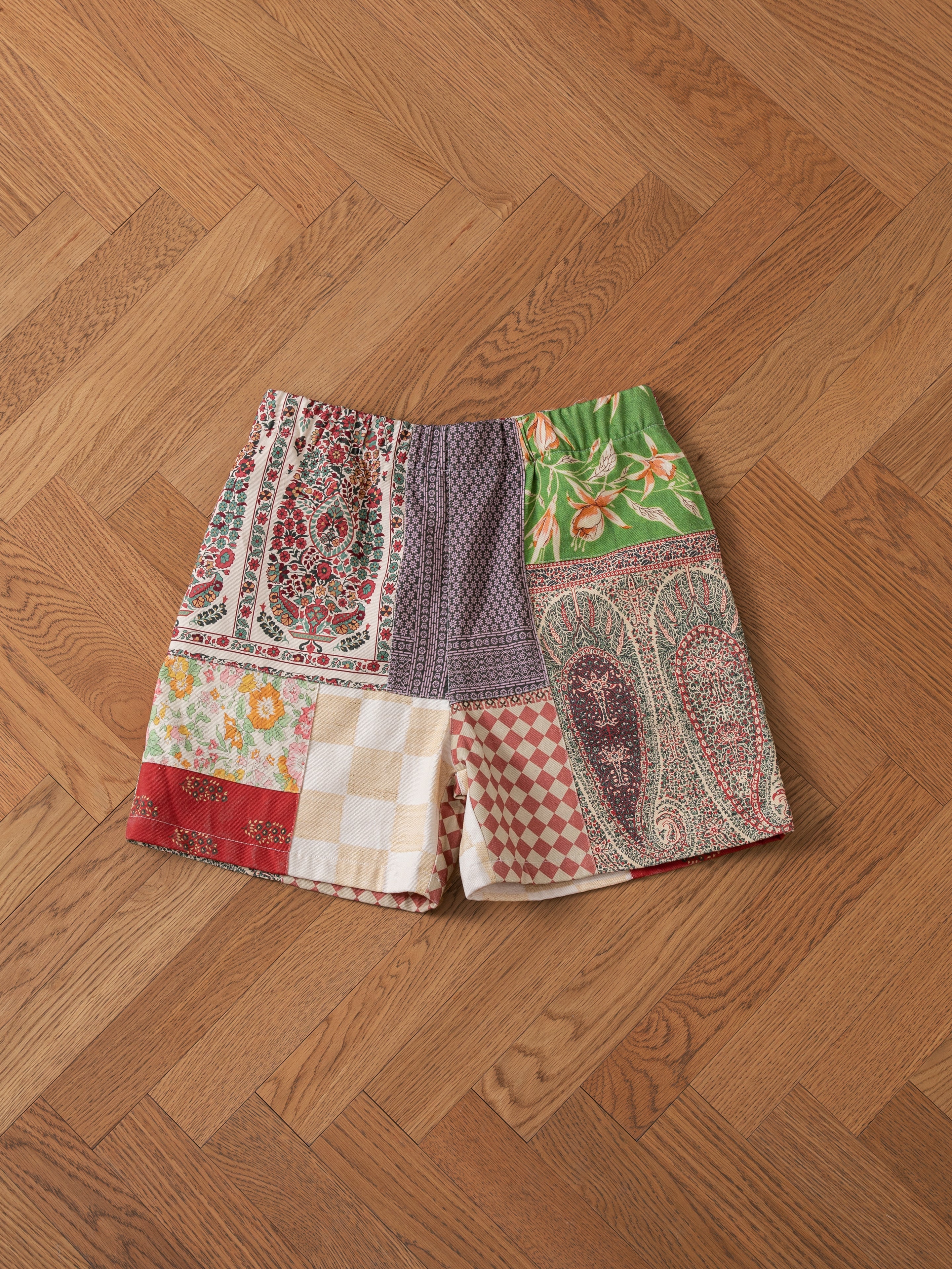 Tapestry Twill Shorts by FOUND, showcasing an array of vibrant patterns, laid flat on a wooden herringbone floor.