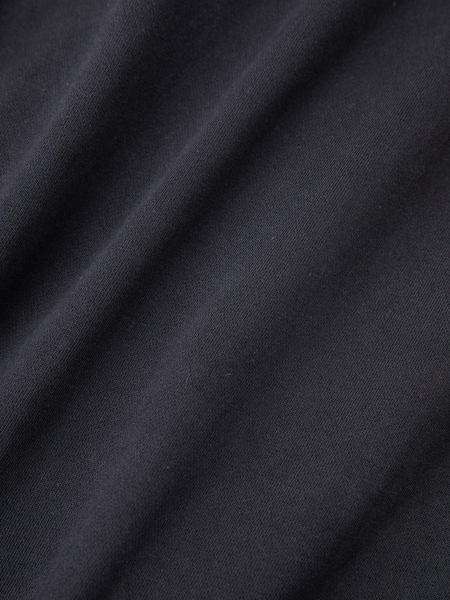 This close-up of the black fabric from the "Tapestry Patchwork Zip Up Hoodie" by FOUND showcases visible folds and texture, echoing a vintage-inspired charm.