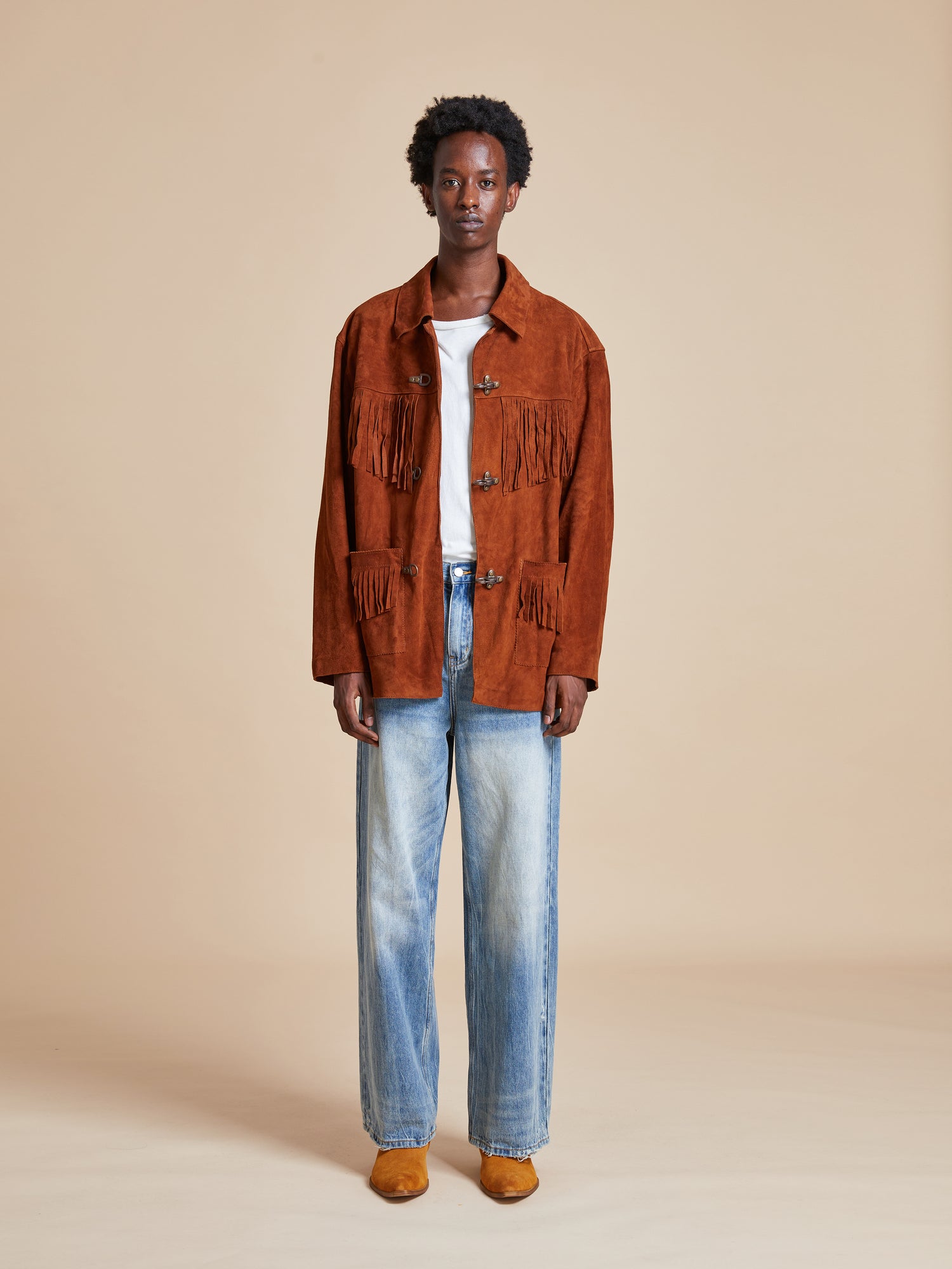 The model is wearing a Found Tobacco Fringe Suede Buckle Jacket and jeans.