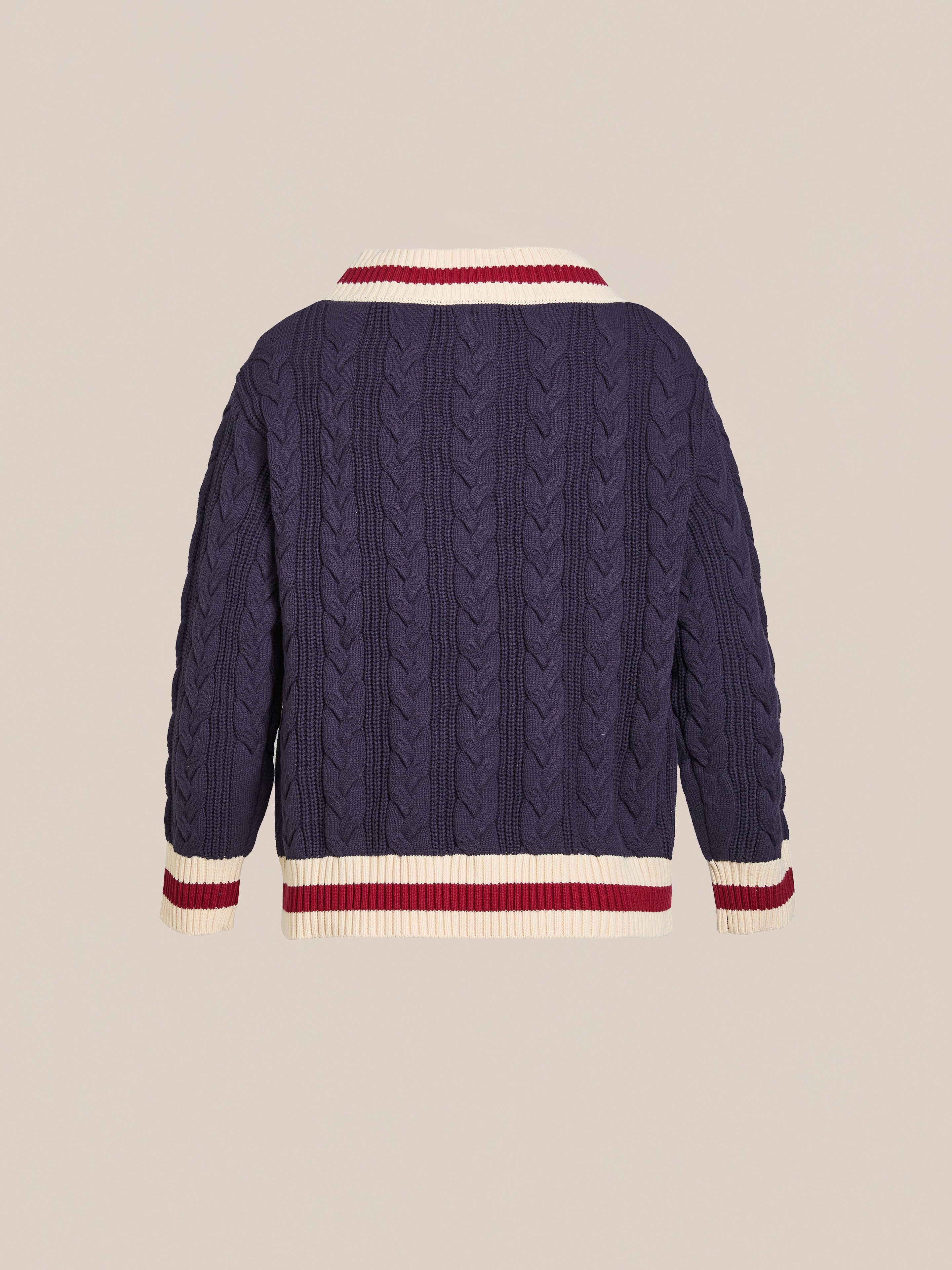 The FOUND V-Neck Cricket Sweater features a navy blue cable-knit design with white and red striped ribbed cuffs and collar, displayed from the back against a beige background.