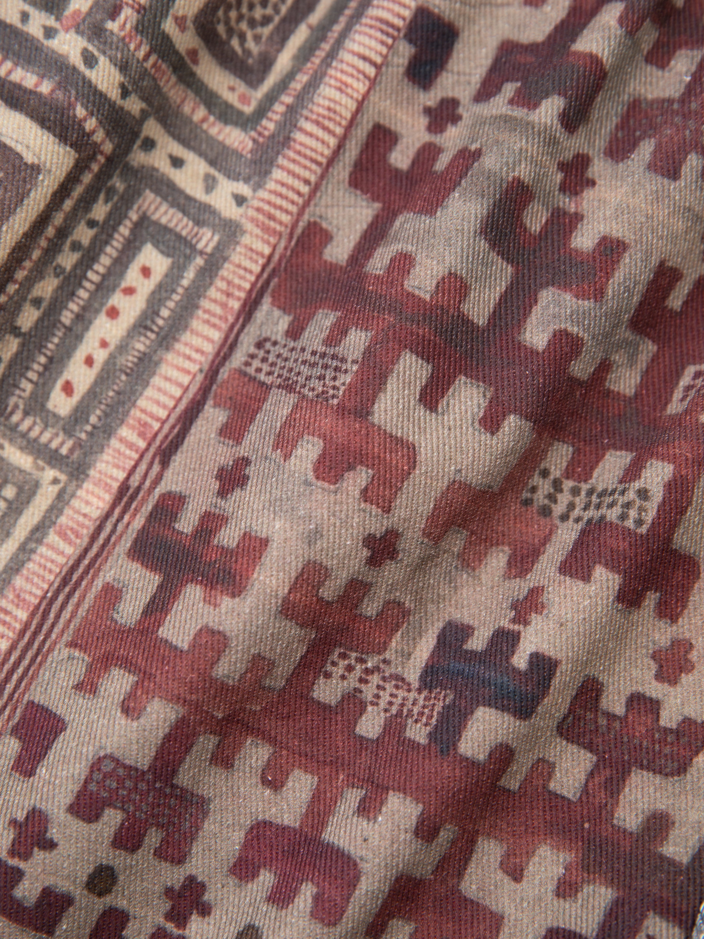 Close-up of the Watercolor Mosaic Work Jacket by FOUND, featuring a fabric with geometric patterns in shades of red, brown, and beige, highlighted by repetitive rectangular and cross-like shapes.