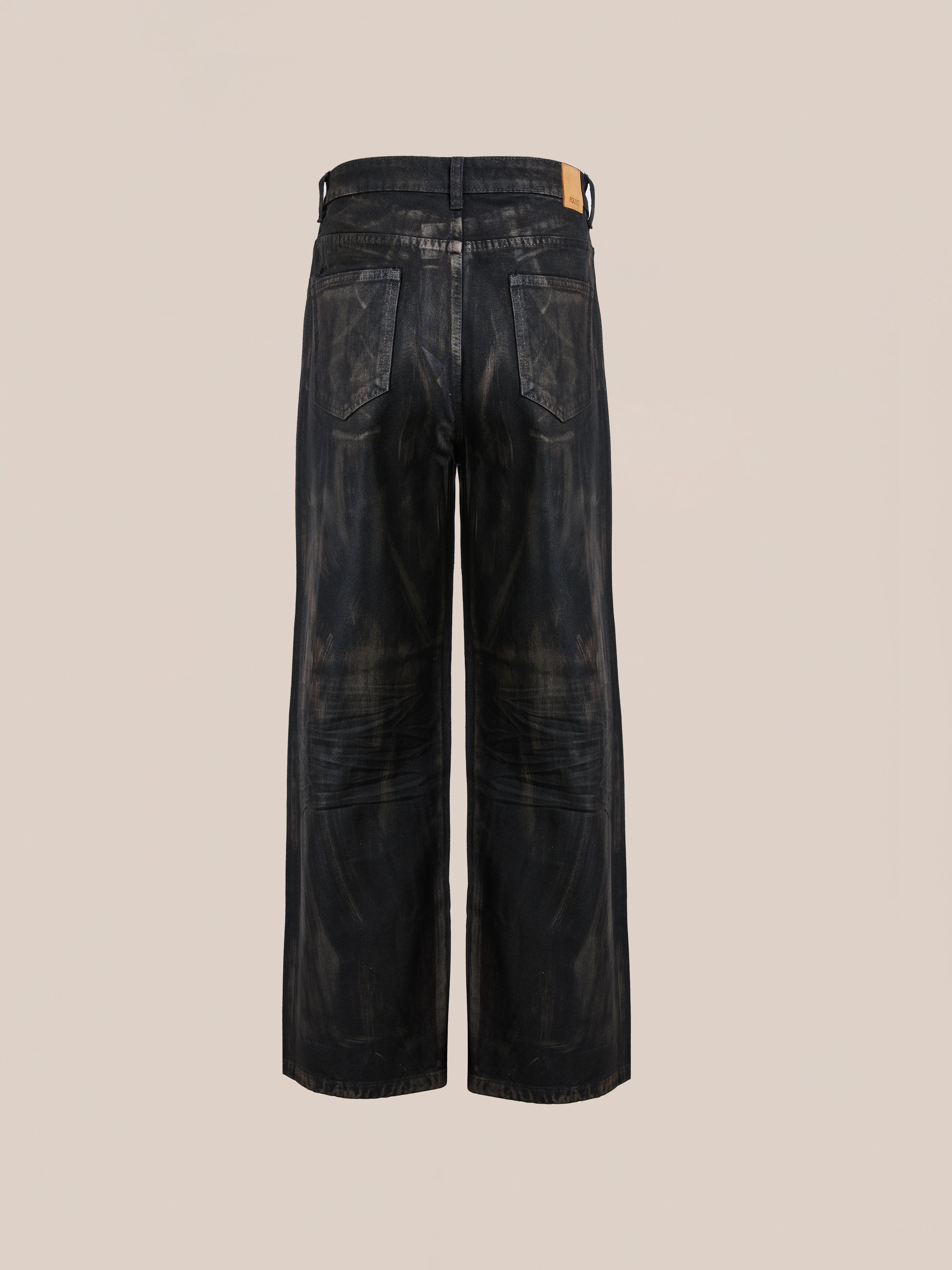 The Waxed Studded Jeans by FOUND are unisex, wide-leg jeans in black with visible fading, a relaxed fit, and a leather waistband patch that highlights vintage craftsmanship against a neutral backdrop.