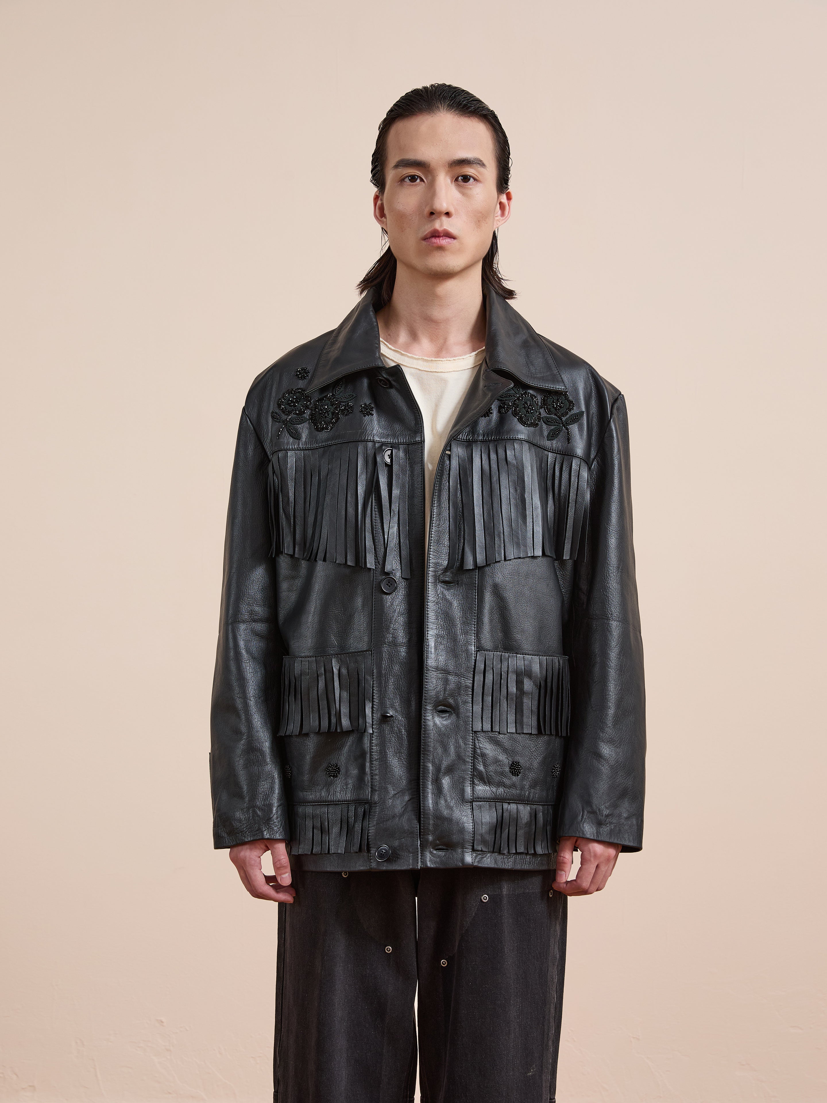 A person stands against a plain background wearing the FOUND Hand Embroidered Leather Fringe Jacket, styled with a white shirt and dark pants.