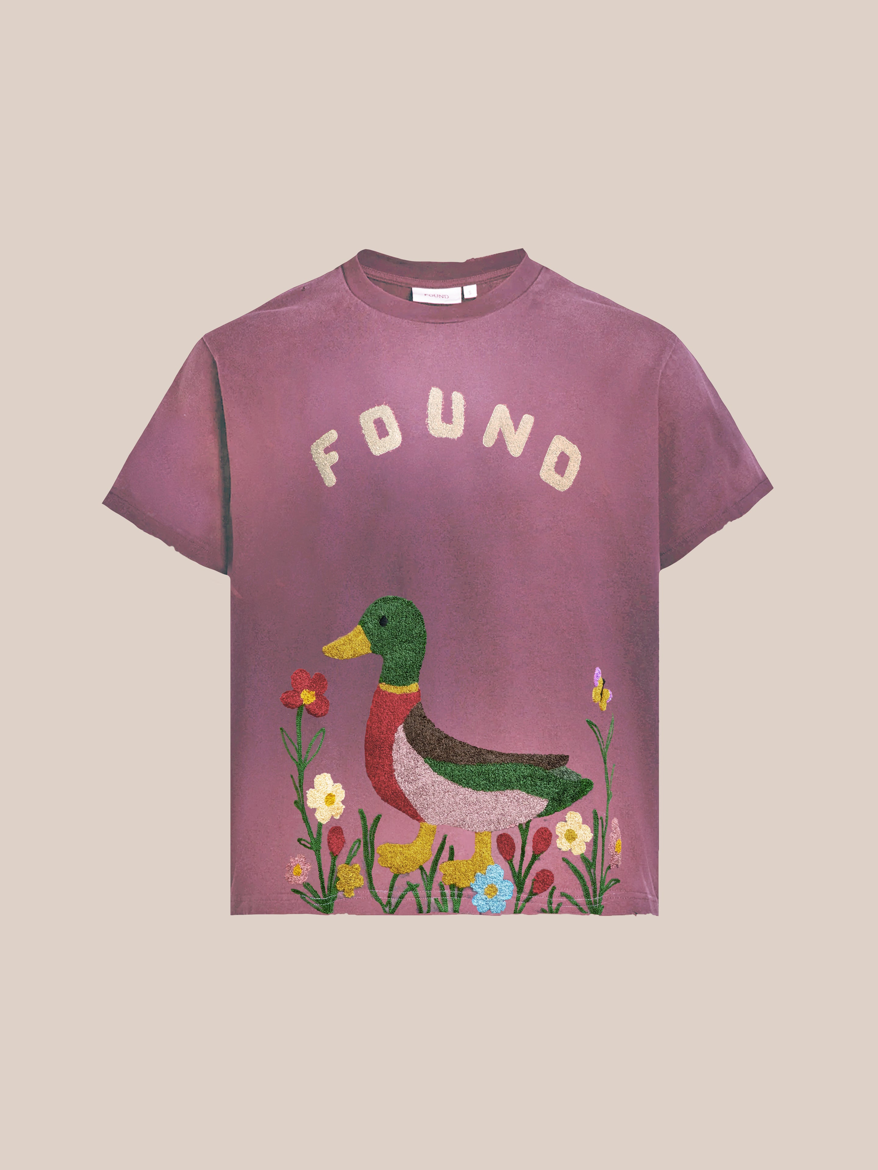 The FOUND Embroidered Wildlife Tee features a duck surrounded by colorful flowers, with "FOUND" above it. This mauve shirt offers a vintage relaxed fit for everyday comfort.