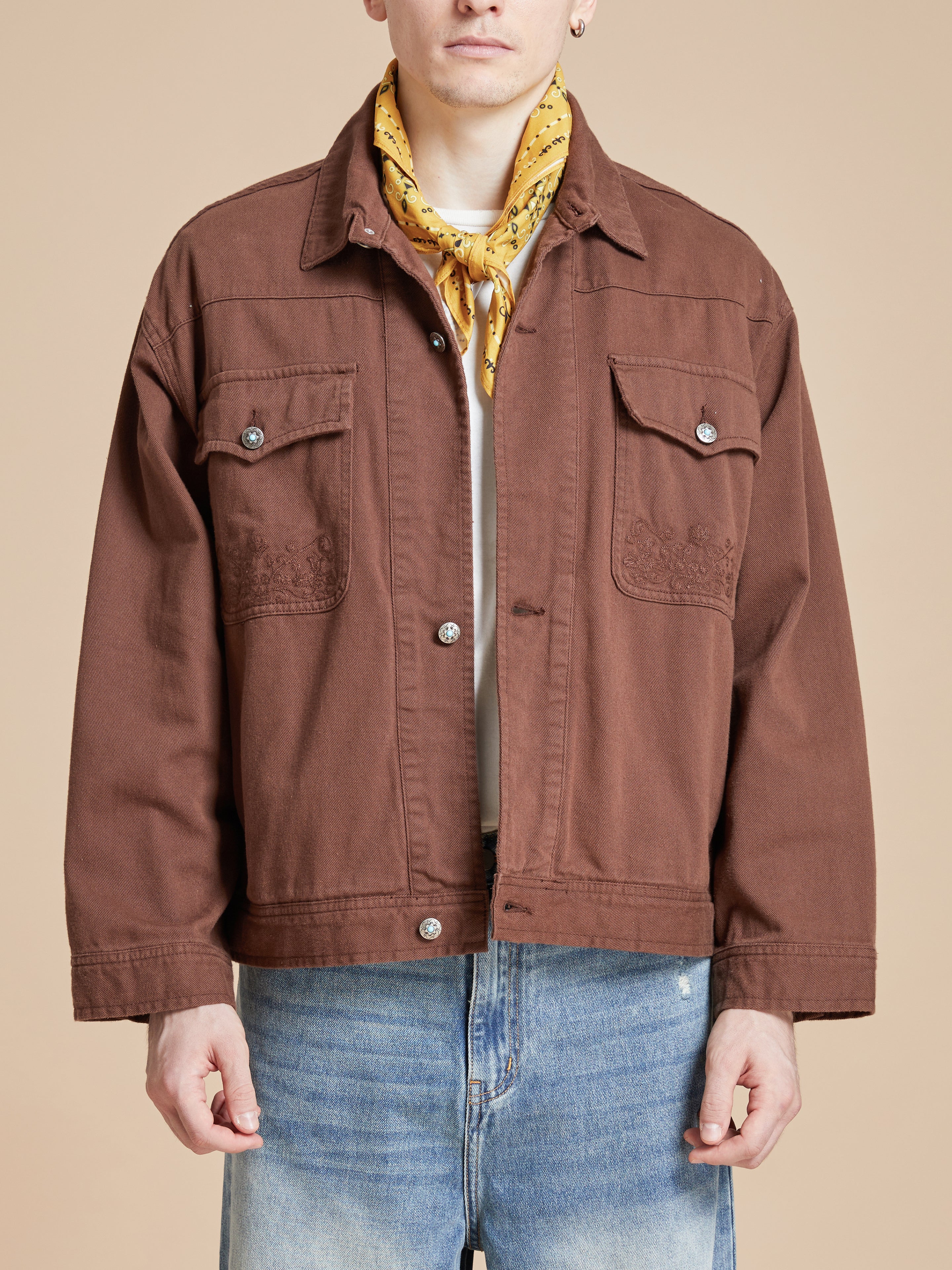 A man wearing a brown jacket and a Found Yellow Western Bandana scarf.