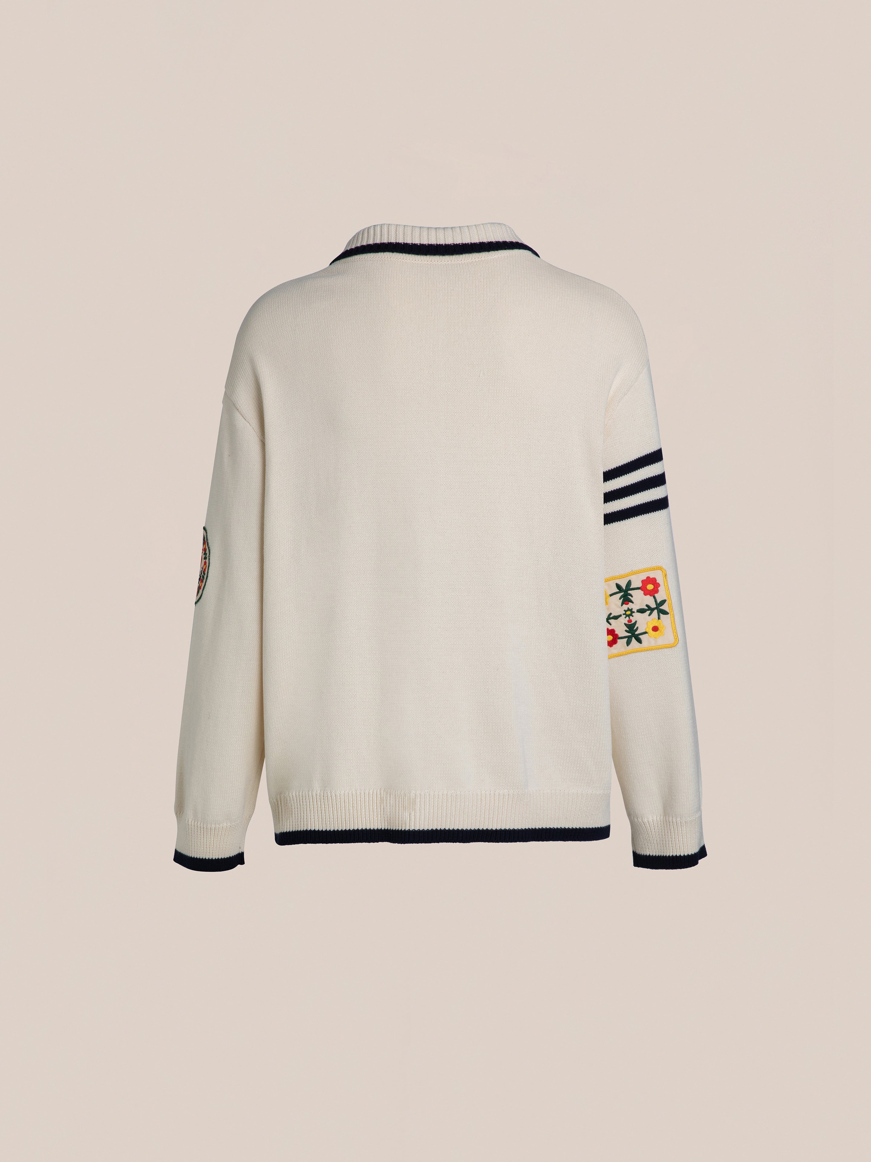 The York Varsity Patch Collared Cardigan by Found features a preppy look with its beige design and black trim, enhanced by three black stripes on the left sleeve and colorful varsity patches on both sleeves against a plain background.