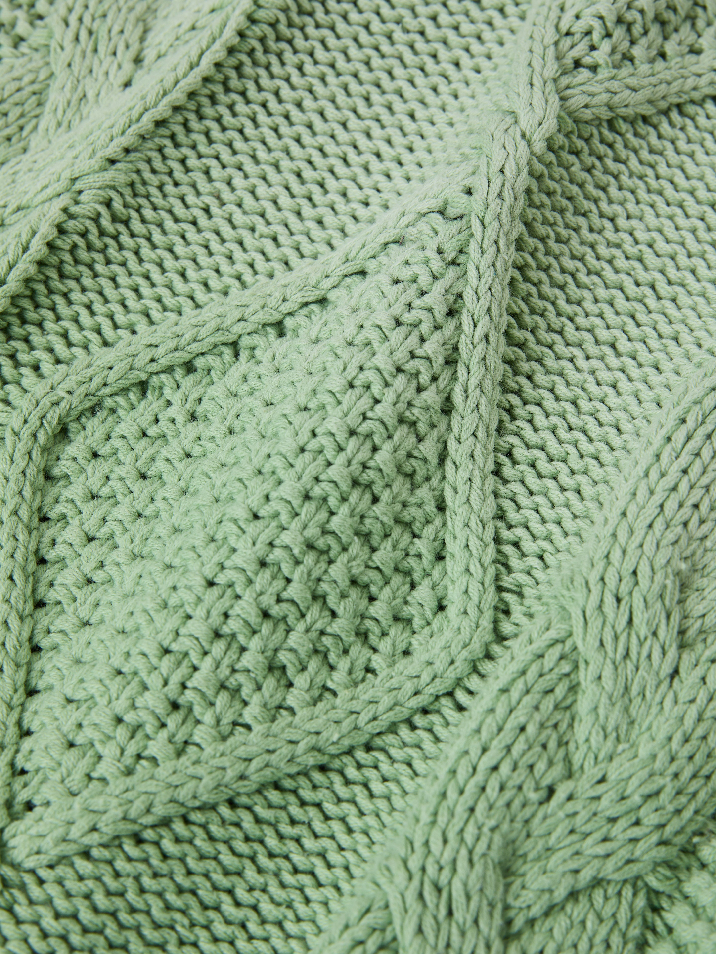 Textured green knit fabric with a diamond pattern and braided details, similar to the intricate design of the heavyweight cotton blend in Found's Zip Up Cable Knit Hoodie.