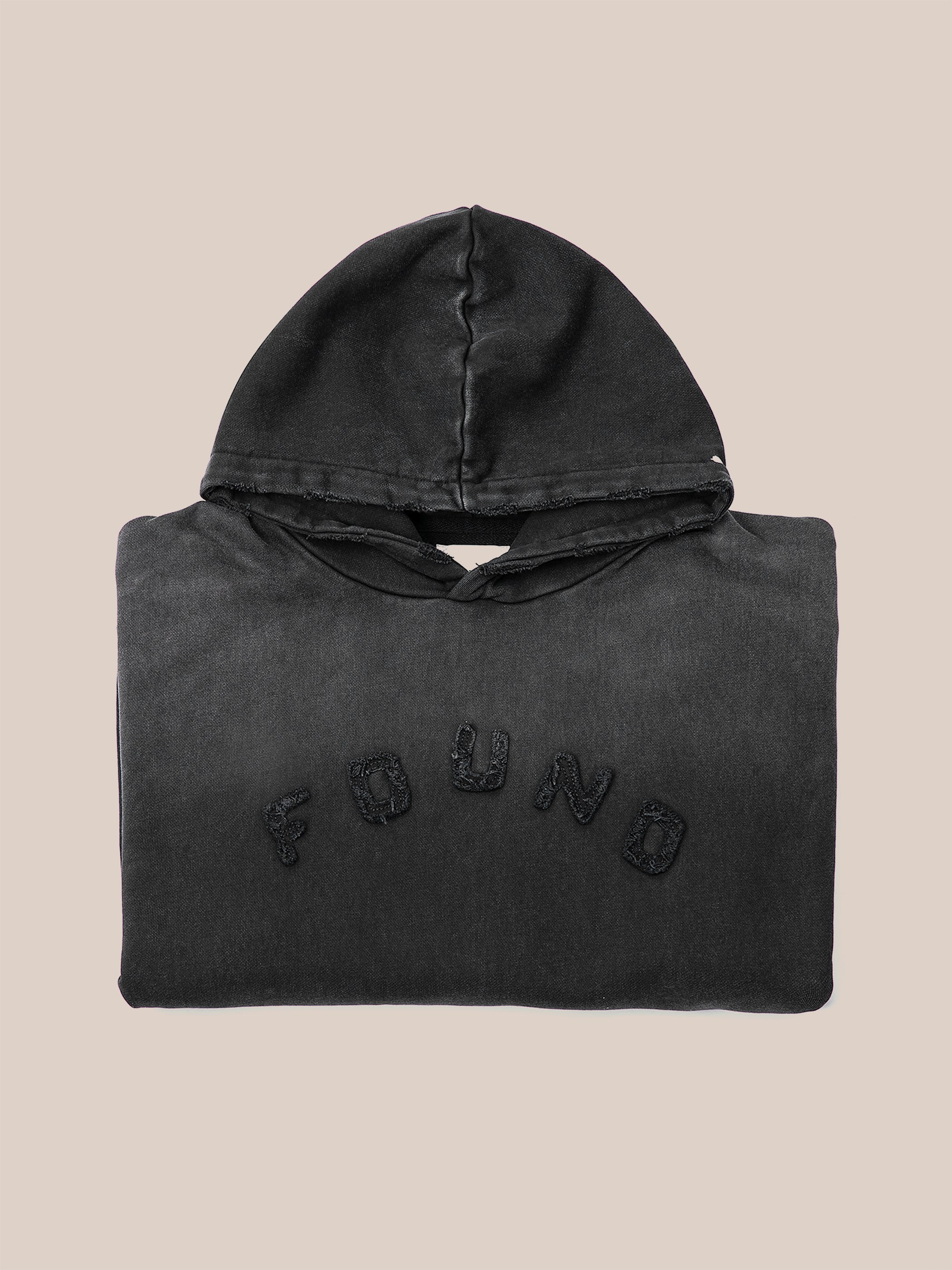 A folded vintage black Logo Patch Hoodie by FOUND, featuring "FOUND" elegantly stitched in capital letters on the front, crafted from soft French terry cotton, set against a plain background.