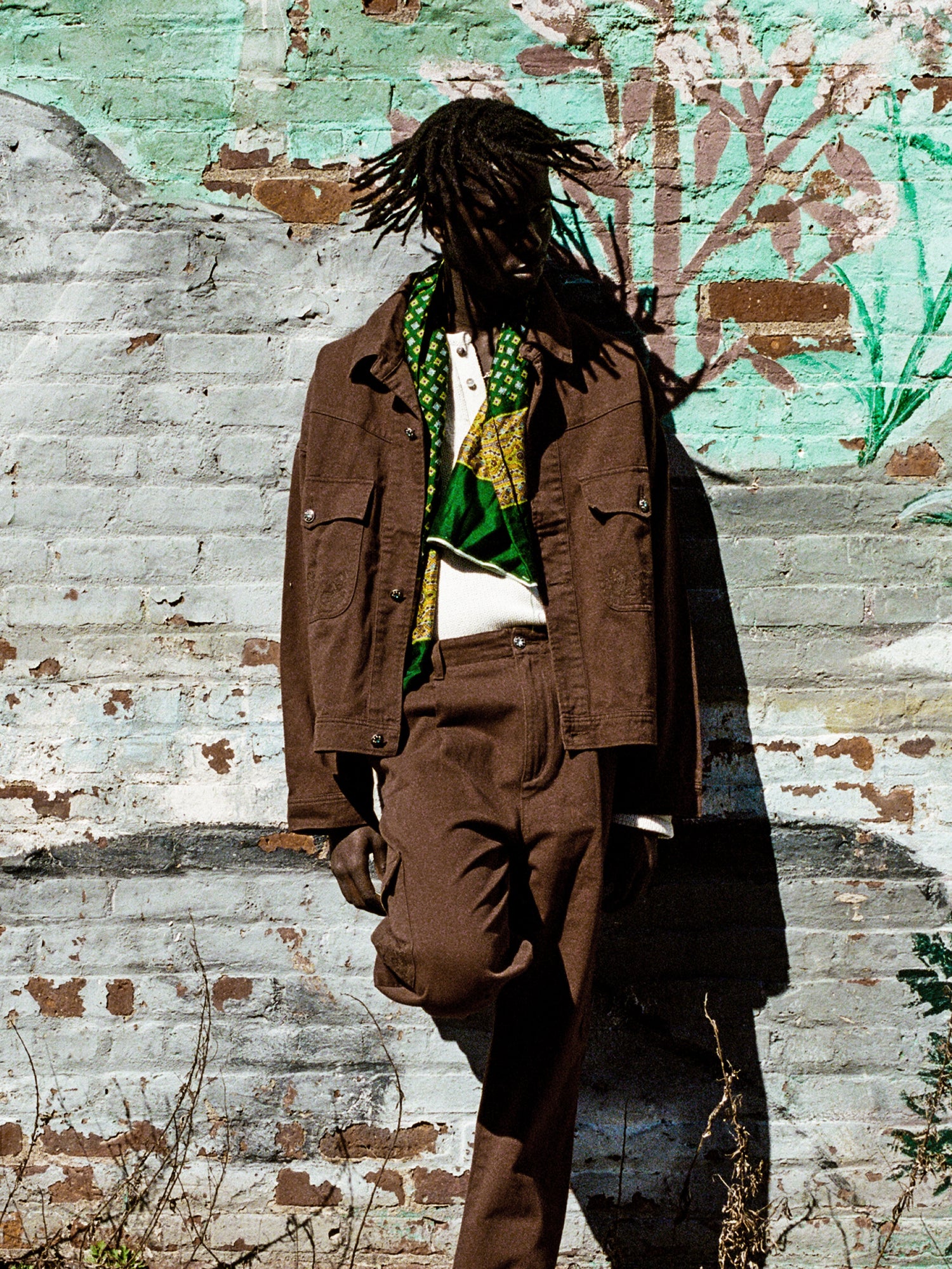 A man with dreadlocks leaning against a classic silhouette brick wall wearing the Found Dusky Western Trucker Jacket.