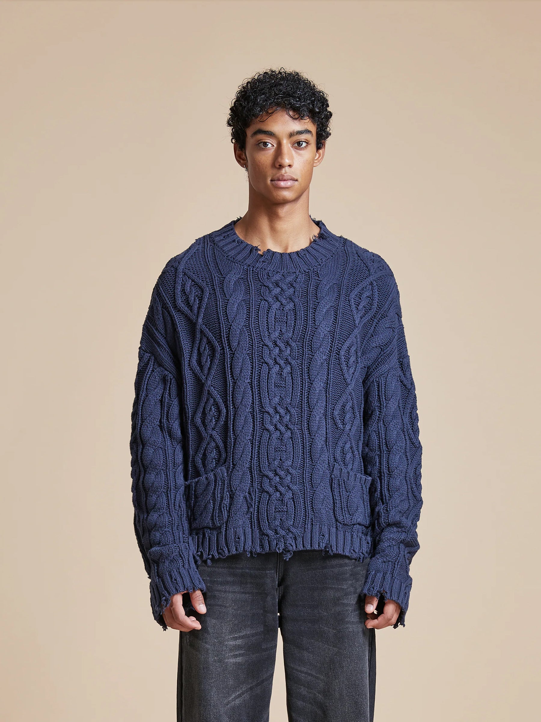 A man wearing a chunky blue cable knit sweater, embodying the softness and warmth of the Found Astral Distressed Cable Knit Sweater.