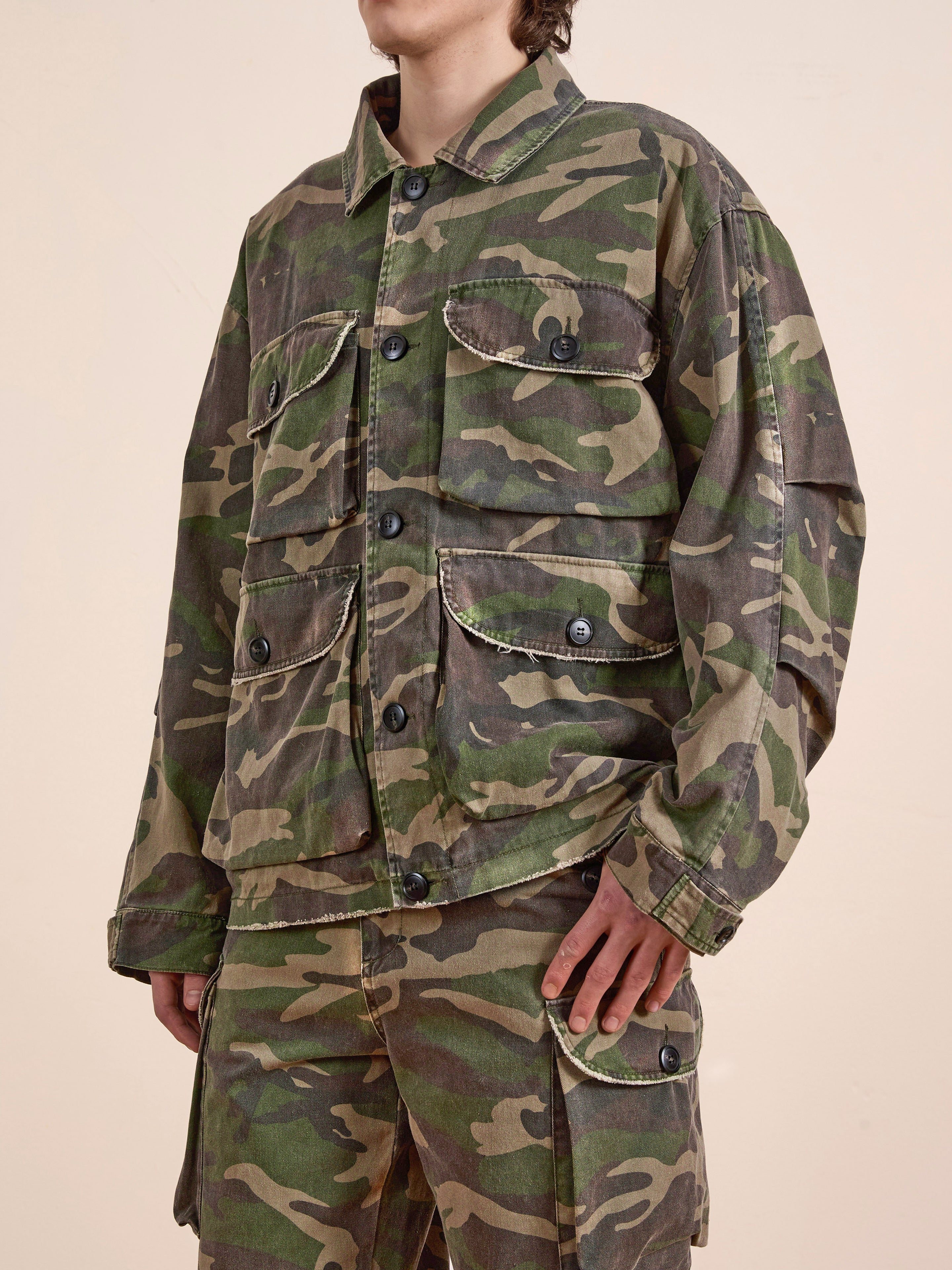 Wearing FOUND's Camouflage Twill Utility Cargo Jacket with matching pants, the individual stands against a neutral backdrop, radiating a vintage vibe with multiple-pocket utility.