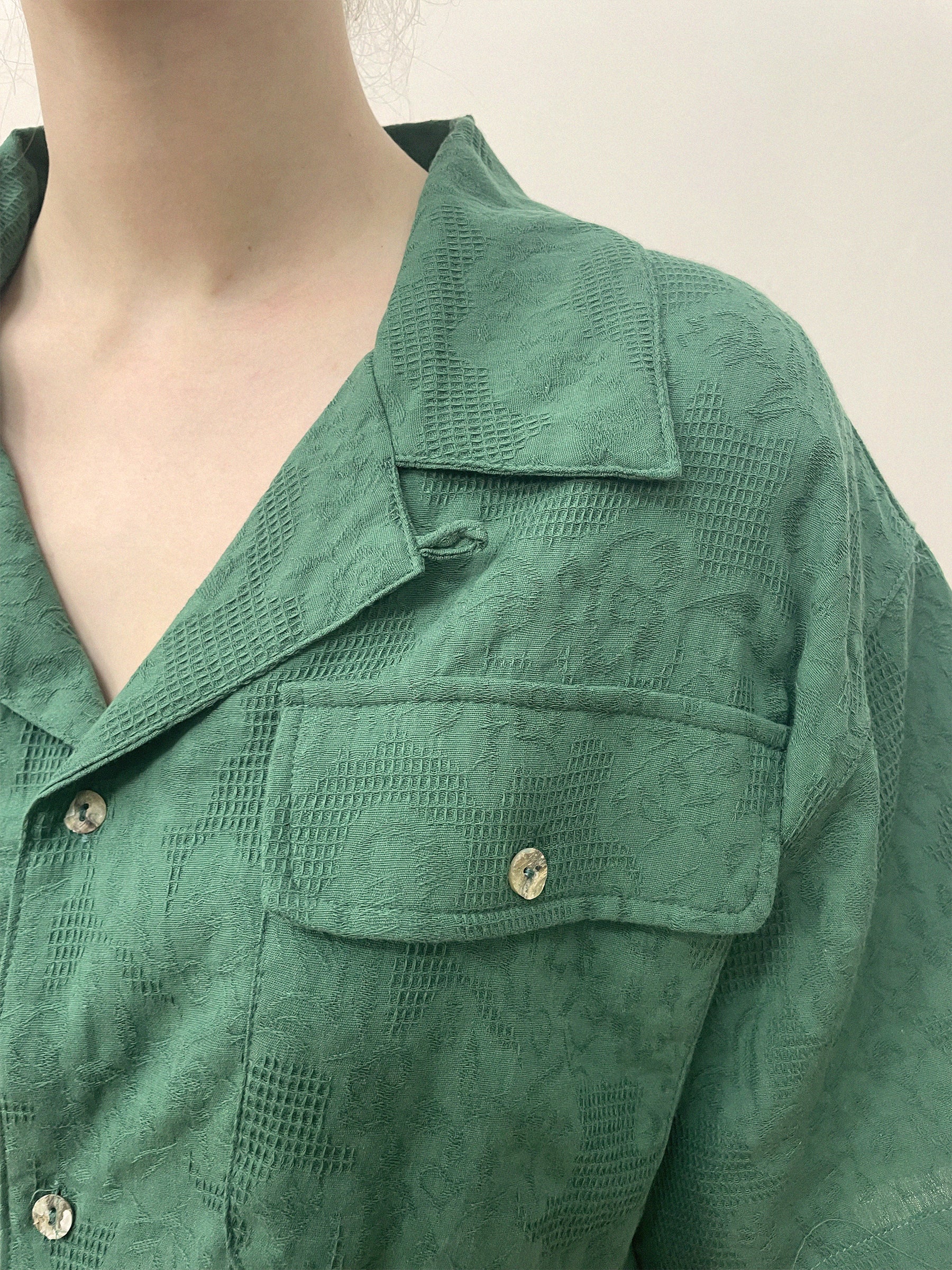 Close-up of a person wearing a green textured Found Mount Camp Shirt with a large collar and a buttoned chest pocket. Made from premium cotton, only the lower half of the person's face and upper torso are visible.