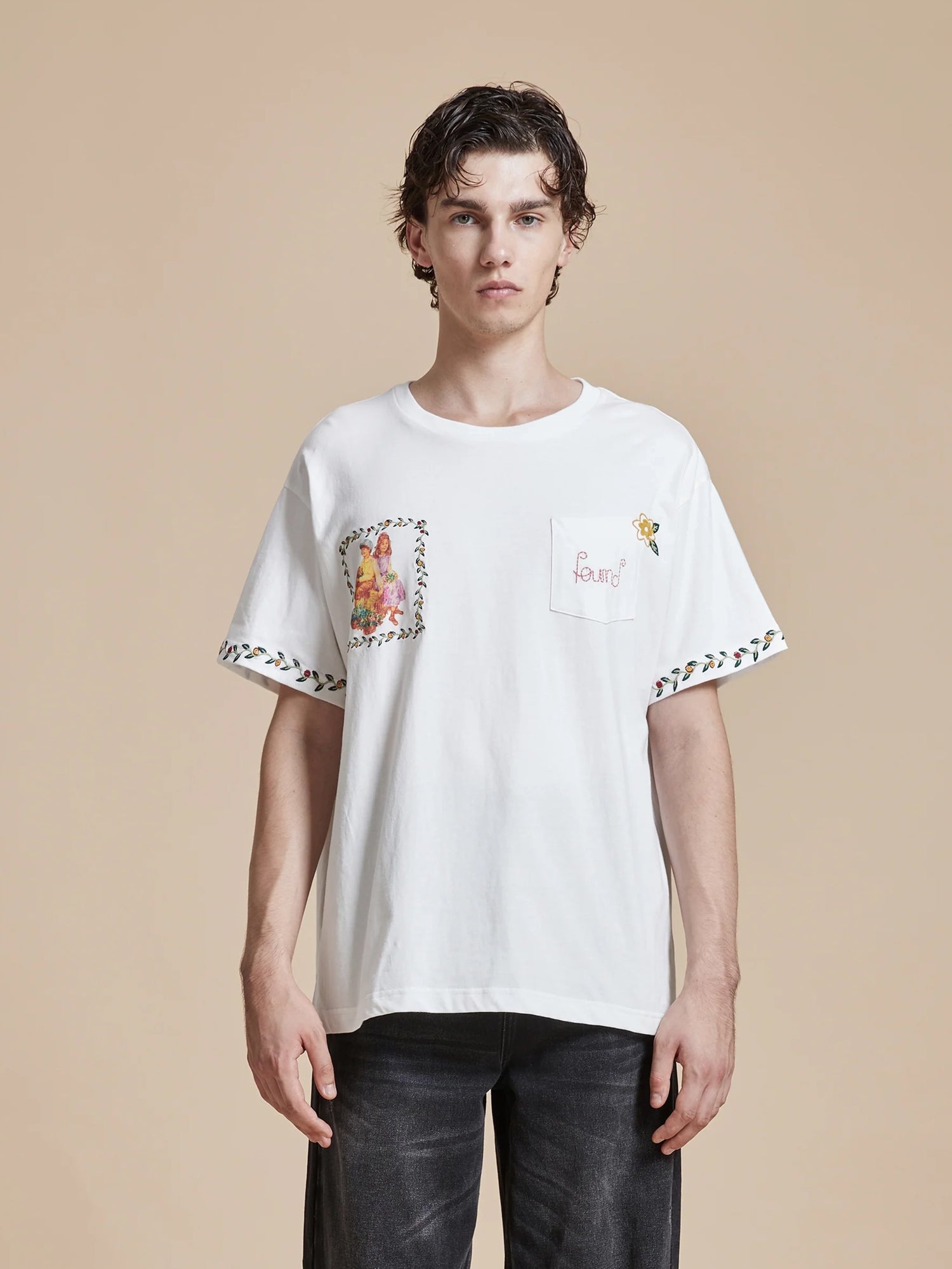 A man wearing a Found Flower Children Tee with an embroidered pocket featuring floral Phulkari style embroideries, showcasing American folk art influence.